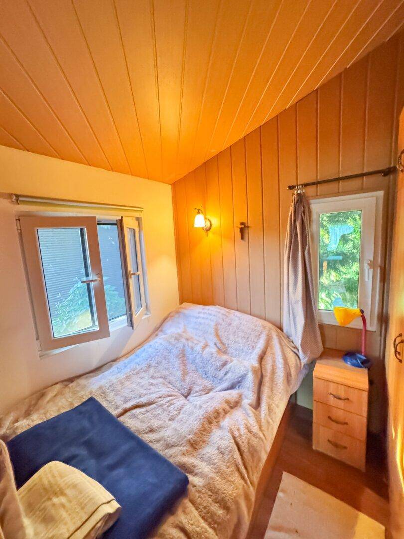 Kleines Schlafzimmer mit Einzelbett, Holzverkleidung und Fenster zum Garten.