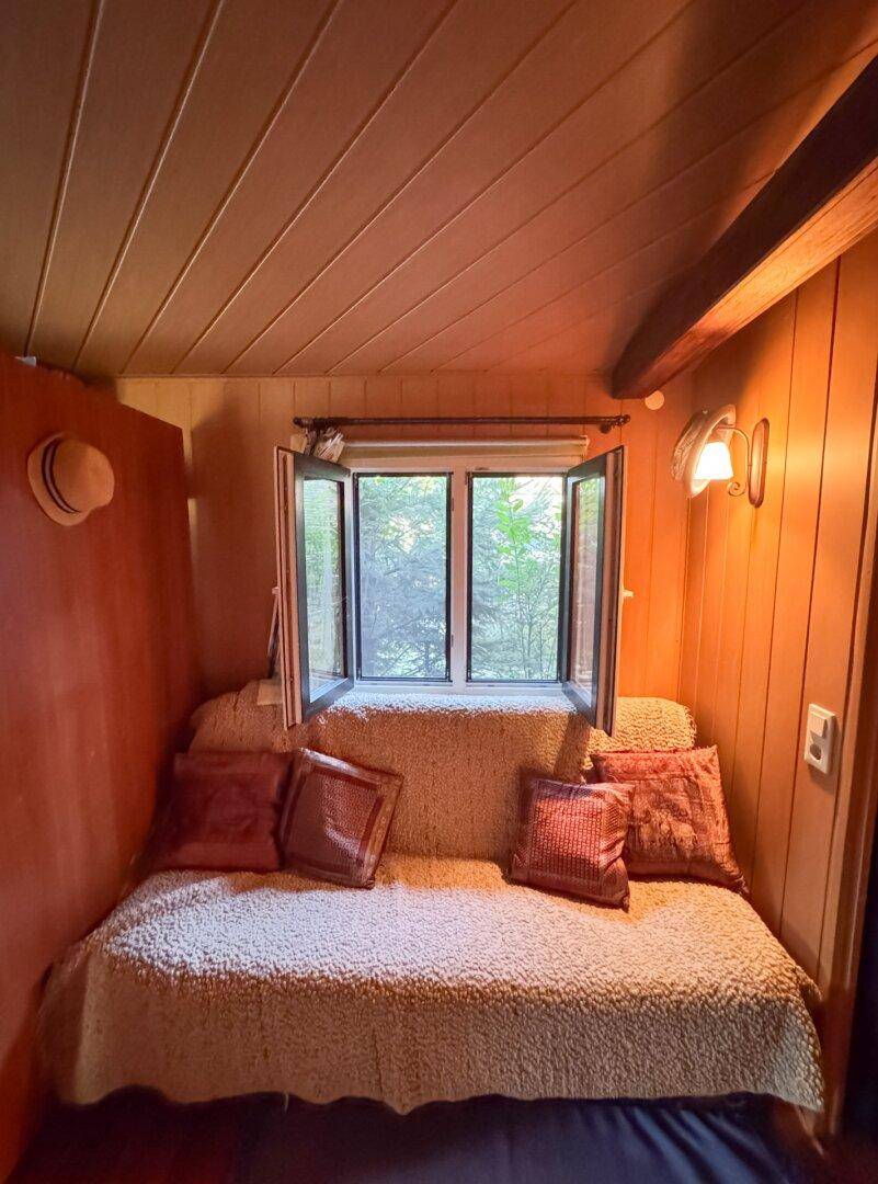 Gemütlicher Schlafbereich mit Tagesbett, Holzverkleidung und geöffnetem Fenster.