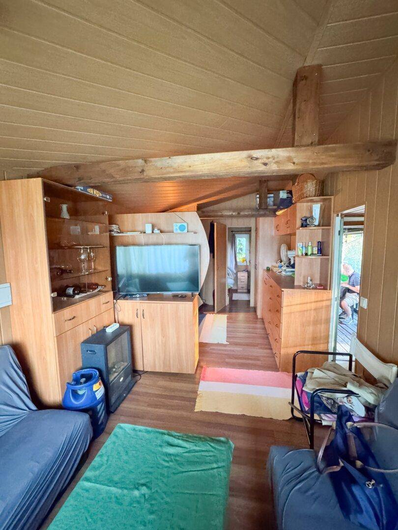 Wohnbereich mit Holzverkleidung, Fernseher und Durchgang zu weiteren Zimmern.