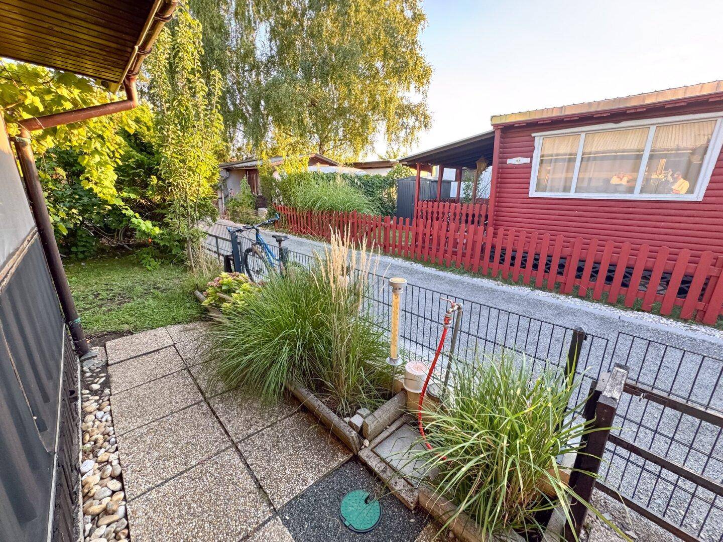Gepflasterter Außenbereich mit Zaun und Blick auf benachbarte Bungalows.