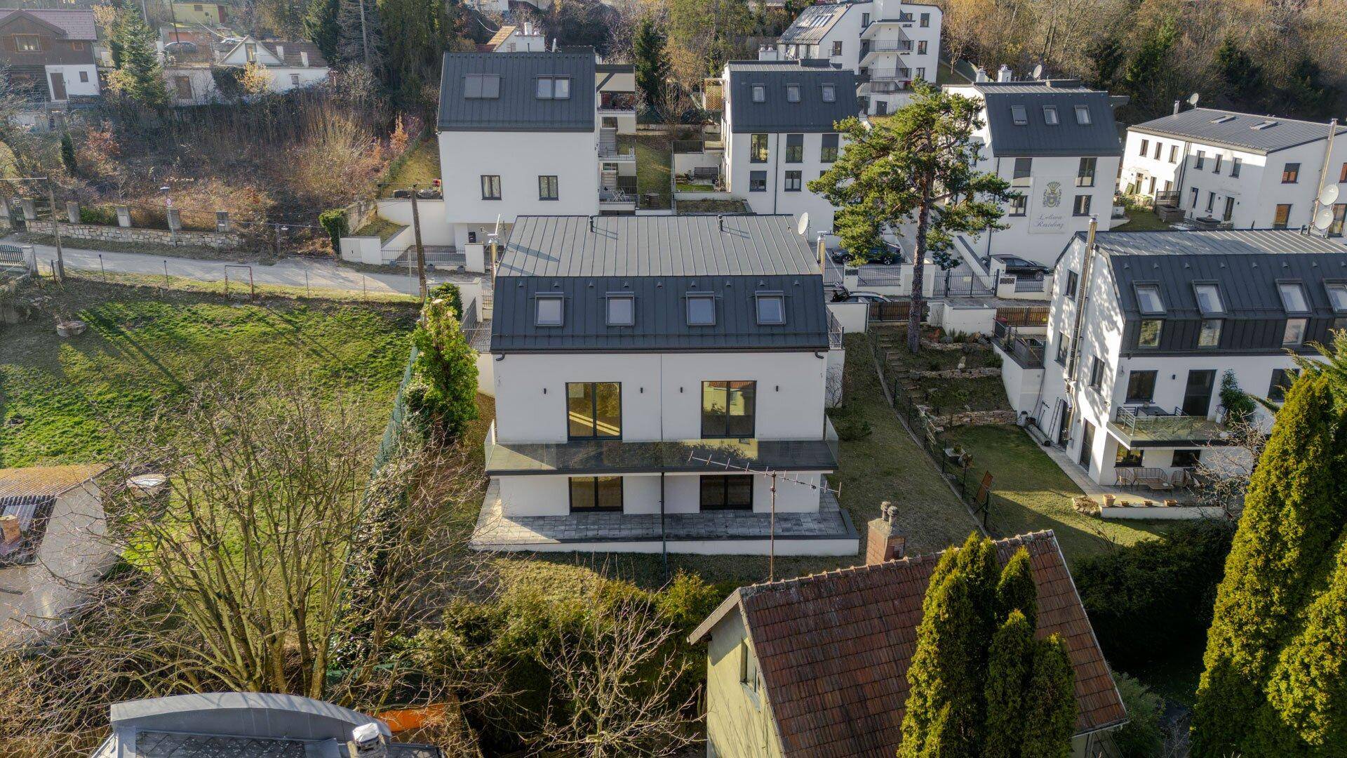 Luftaufnahme der modernen Reihenhäuser in einer grünen, hügeligen Landschaft.