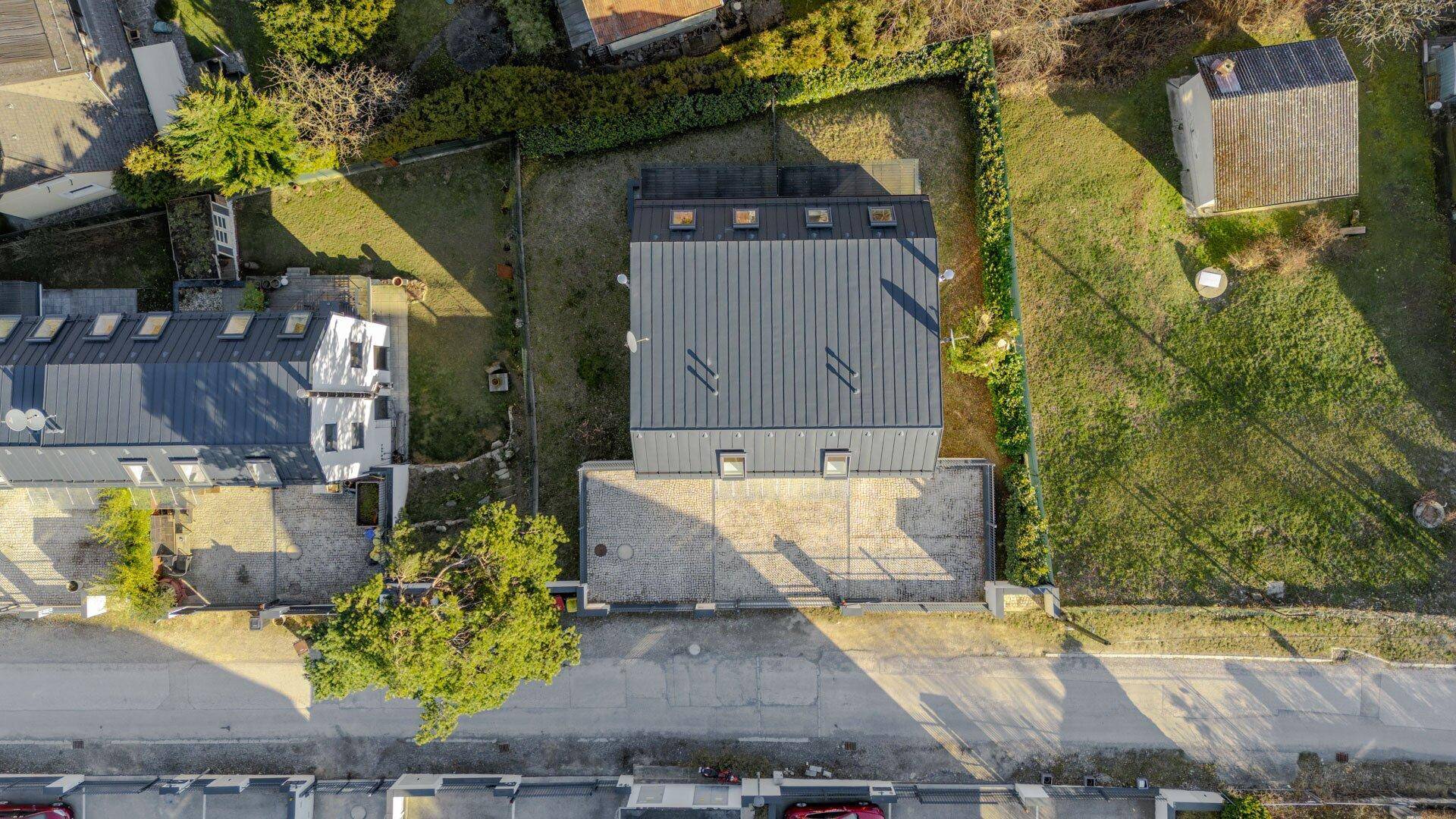 Draufsicht auf das Gebäude mit Mansarddach und gepflastertem Vorplatz, umgeben von Gärten.