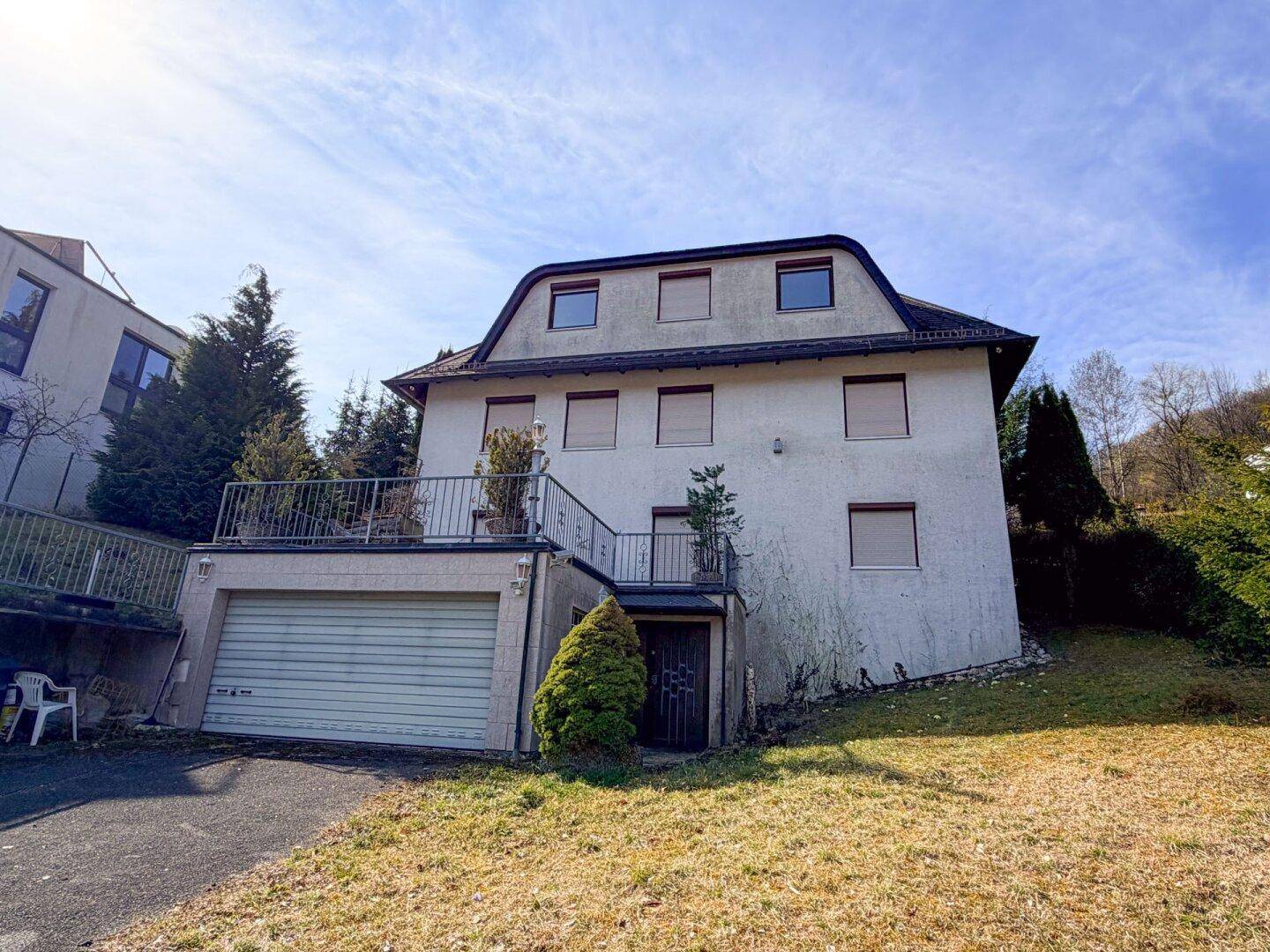 Freistehendes Wohnhaus mit Garage, Terrasse und großem Gartenbereich unter blauem Himmel.