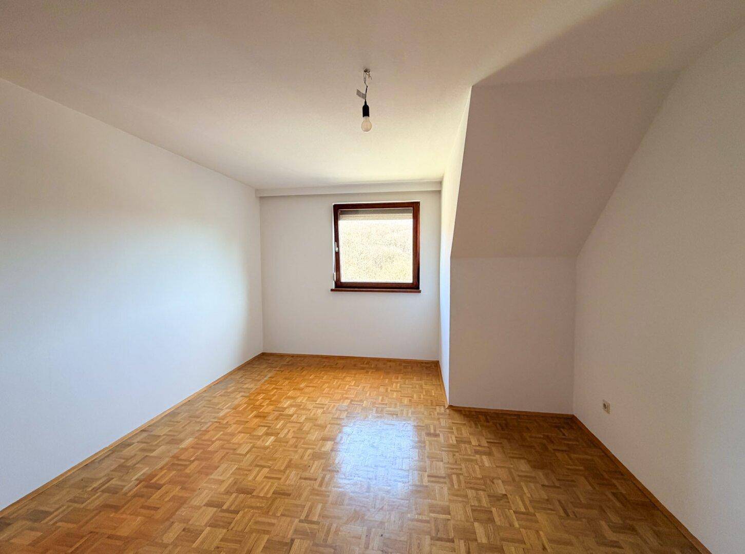 Helles Zimmer mit Parkettboden und Dachschräge, bereit zur individuellen Gestaltung.