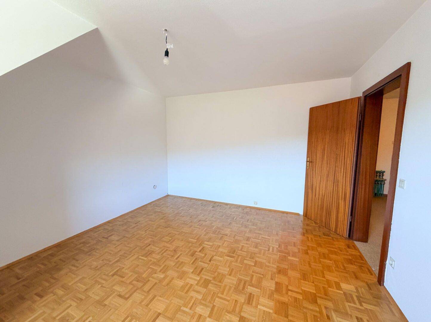 Geräumiges Zimmer mit Parkettboden und Holztür, ideal für Schlaf- oder Arbeitsbereich.
