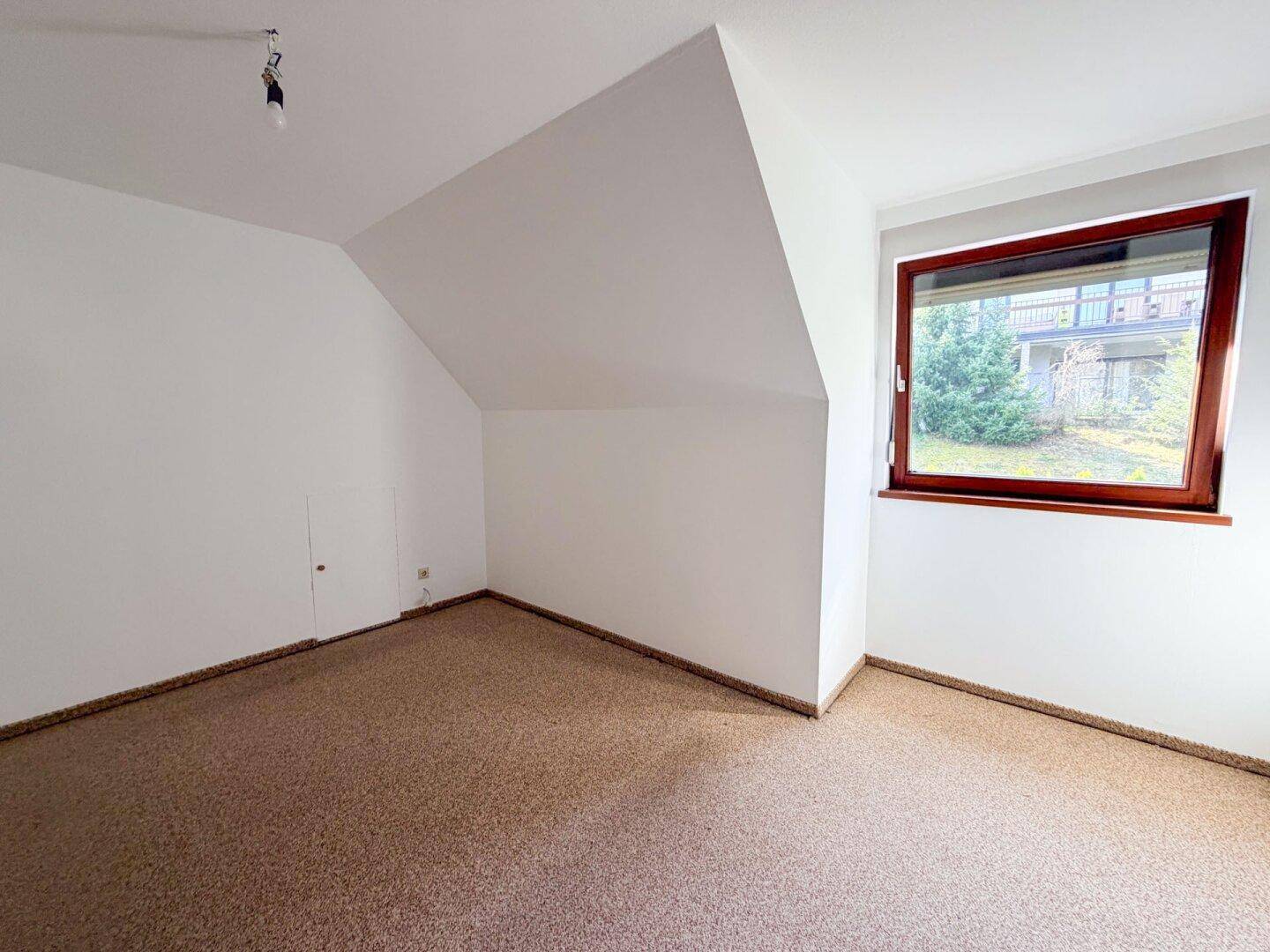 Helles Zimmer mit Teppichboden und Dachschräge, bietet Potenzial für gemütliches Wohnen.