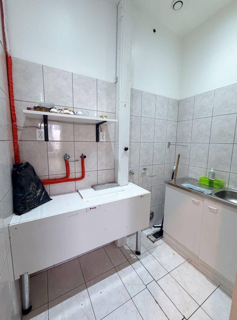Kleine Küchenzeile mit Spülbecken, Fliesenboden und gefliesten Wänden, ideal für Pausen oder Vorbereitung.