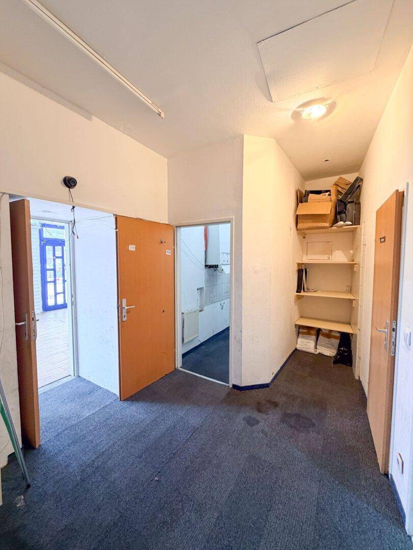 Hinterer Bereich mit Teppichboden, mehreren Türen und Regalen, der als Lager oder Büro genutzt werden kann.