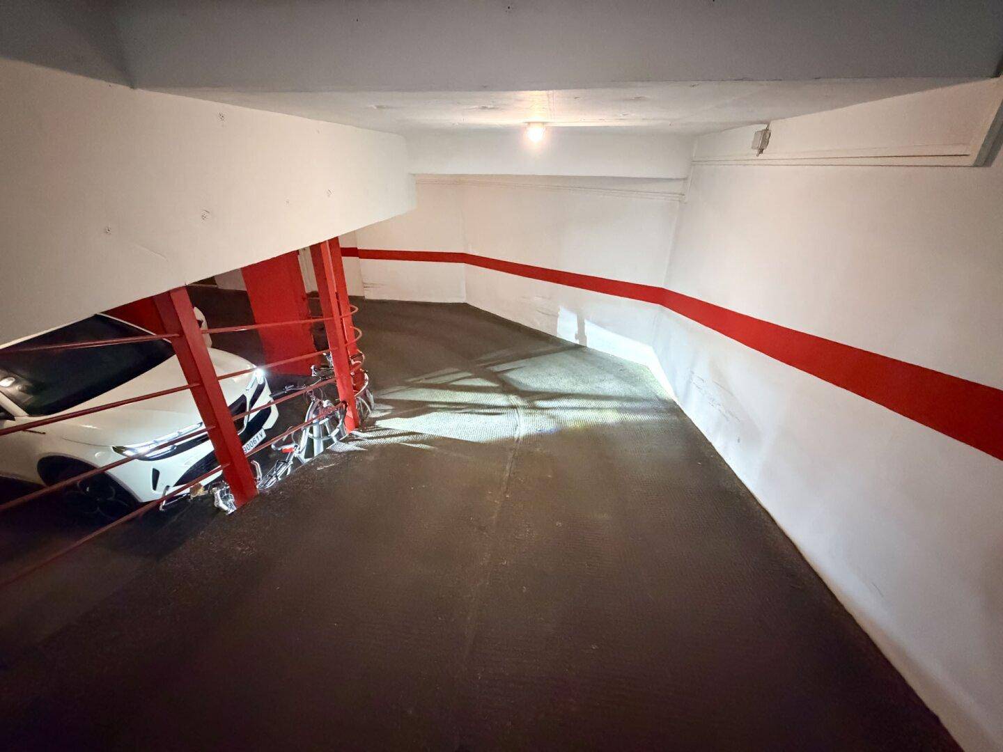 Kurvige Rampe in der Tiefgarage mit roten Säulen und einem geparkten Auto.