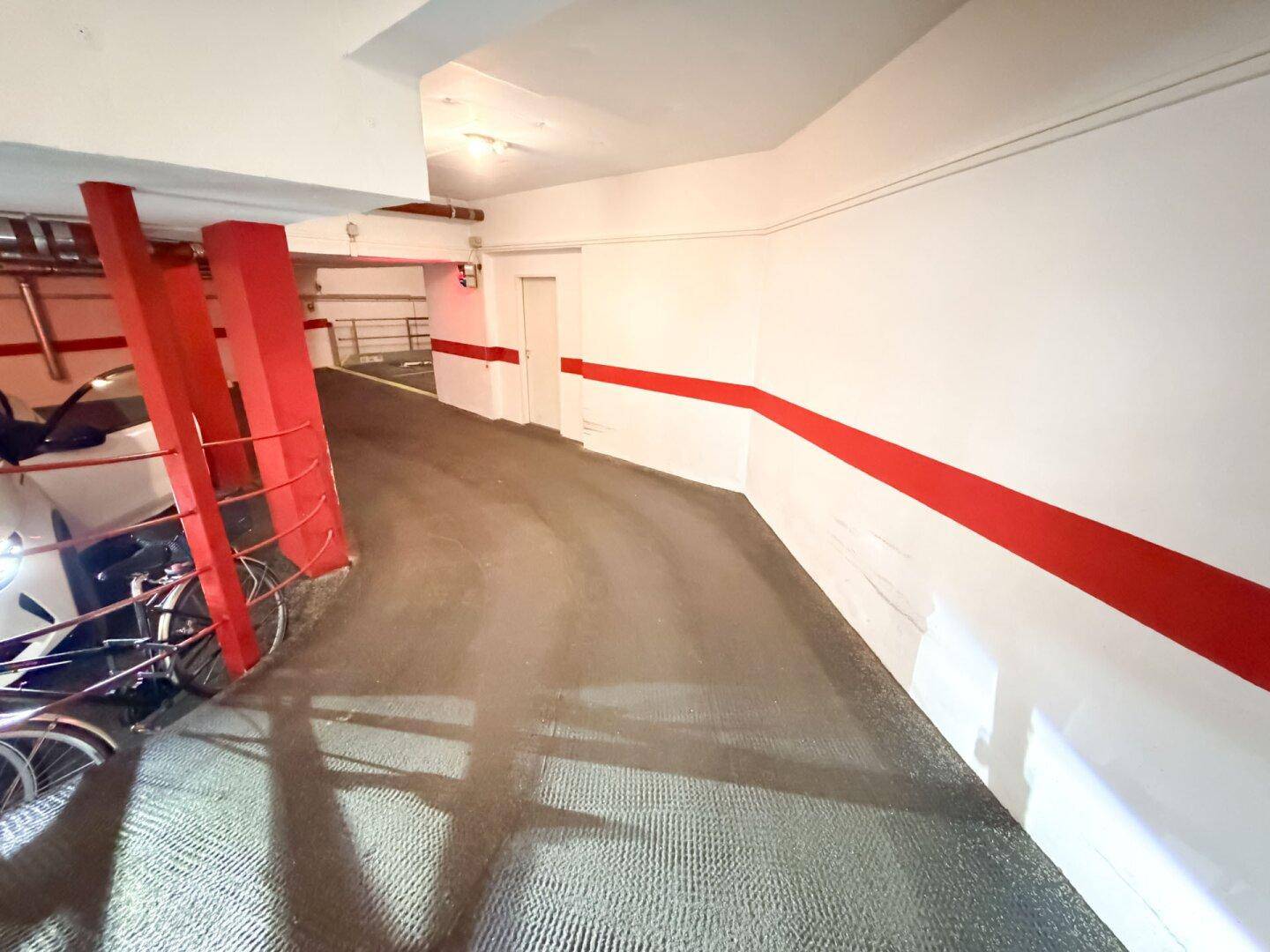 Geschwungene Rampe in der Tiefgarage mit geparktem Auto und Fahrrädern.