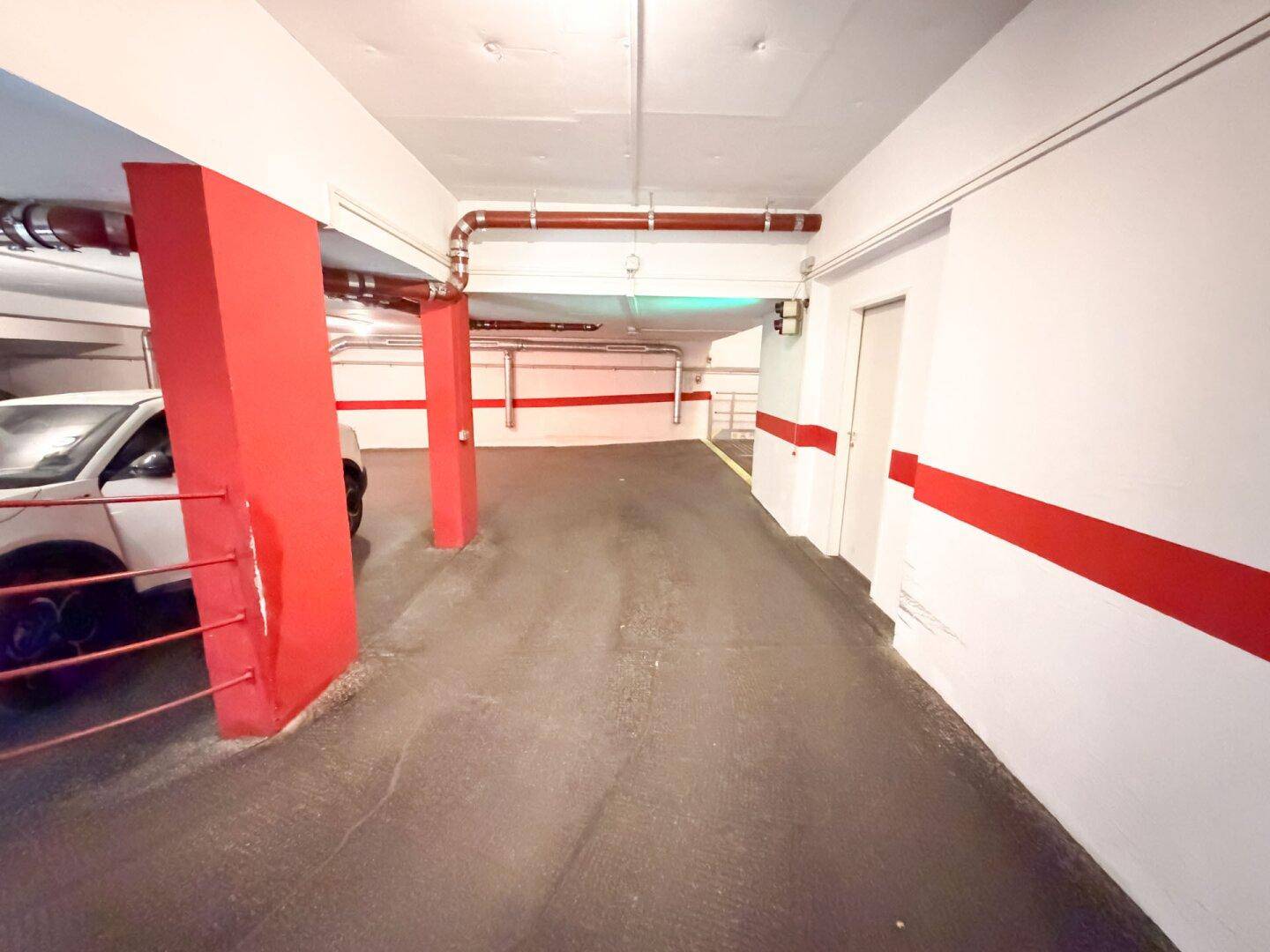 Tiefgaragenbereich mit roten Säulen, einem geparkten Auto und sichtbaren Installationen.