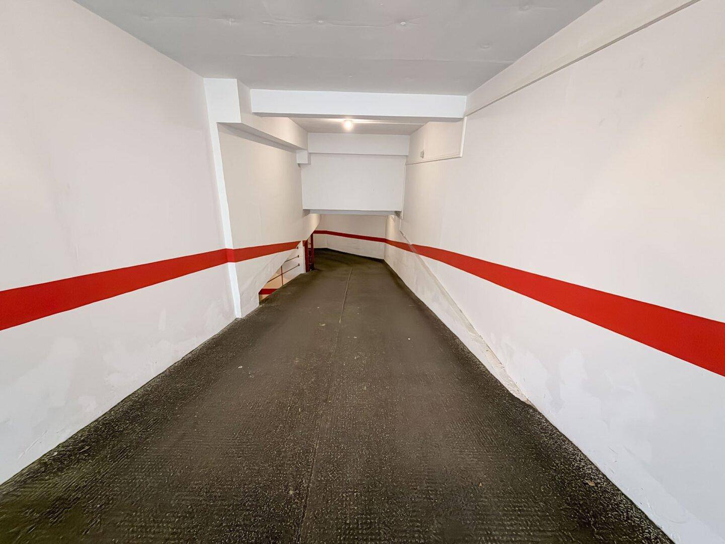 Einfahrt zur Tiefgarage mit Rampe und roten Markierungen an den weißen Wänden.