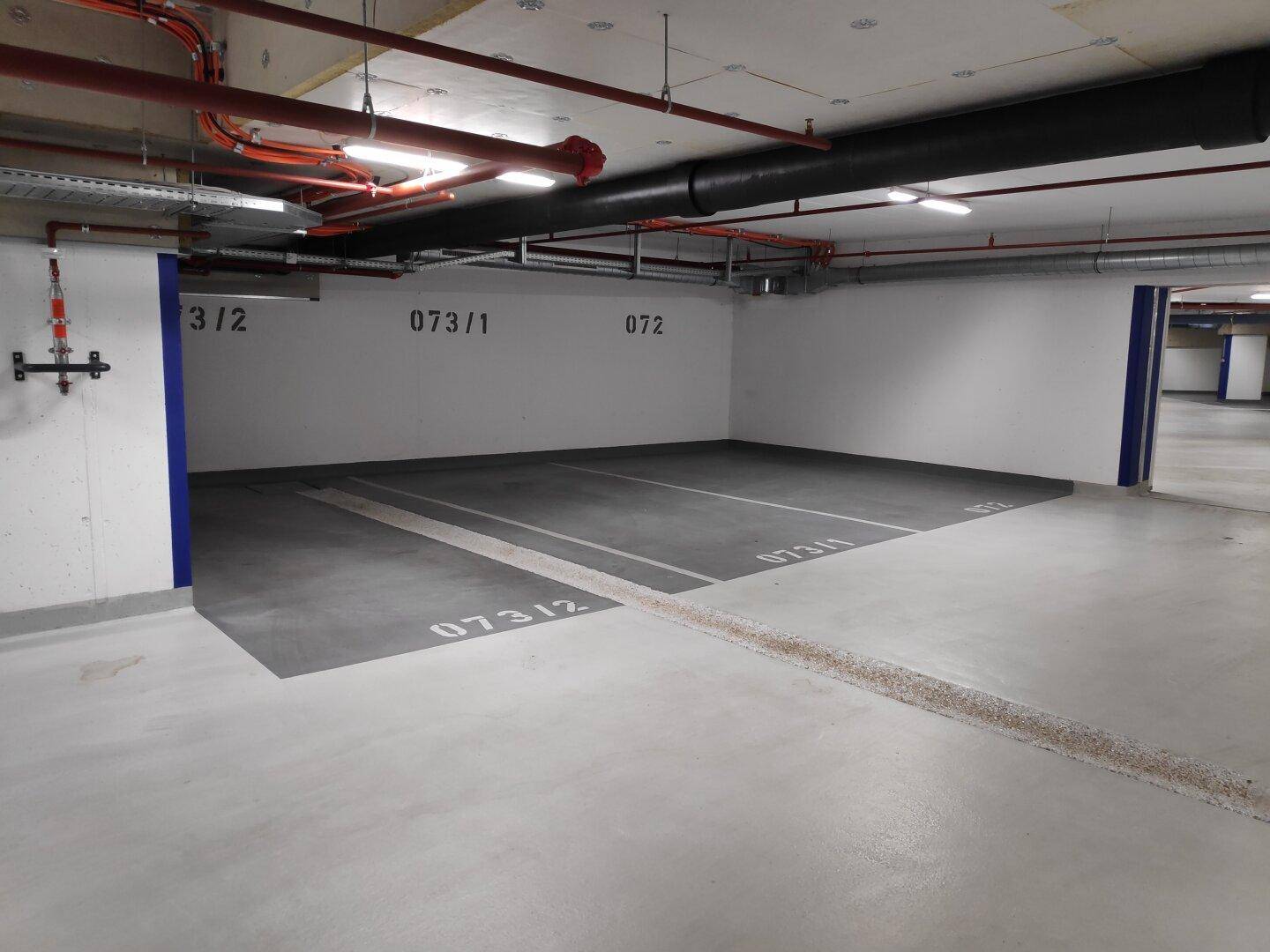 Tiefgaragenstellplatz mit Betonboden und sichtbaren Leitungen an der Decke in einem modernen Gebäude.