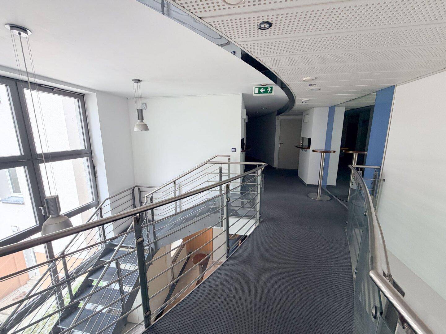 Moderner Flur mit Treppenhaus, Teppichboden und Metallgeländer.
