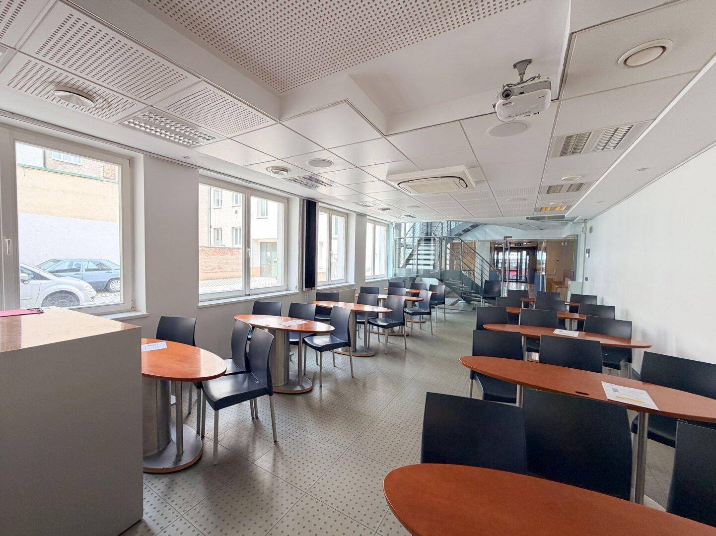 Großer Schulungsraum mit vielen Tischen, Stühlen und einem Beamer an der Decke.