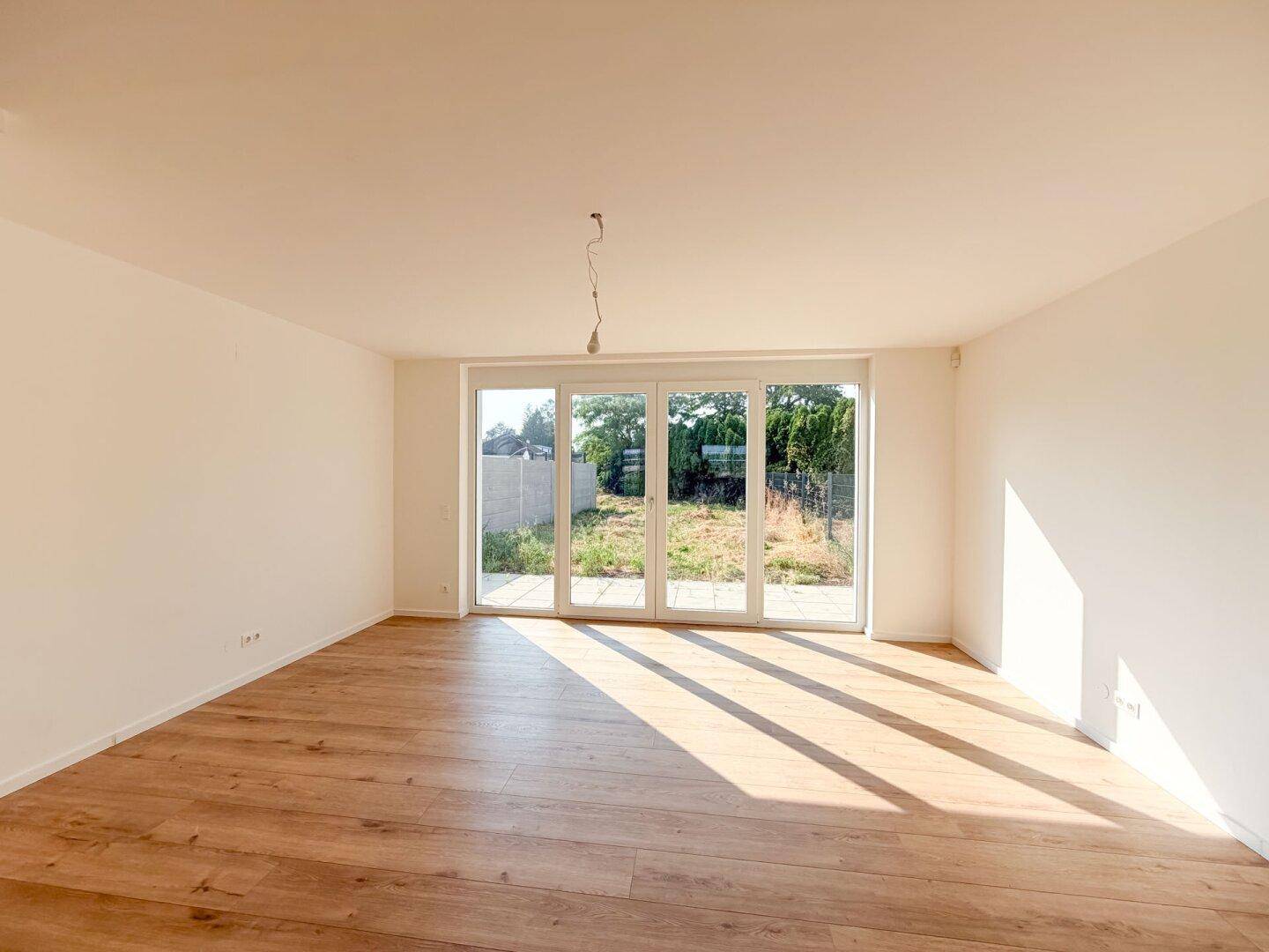 Lichtdurchfluteter Wohnraum mit Holzboden und großen Glastüren, die zum Garten führen.