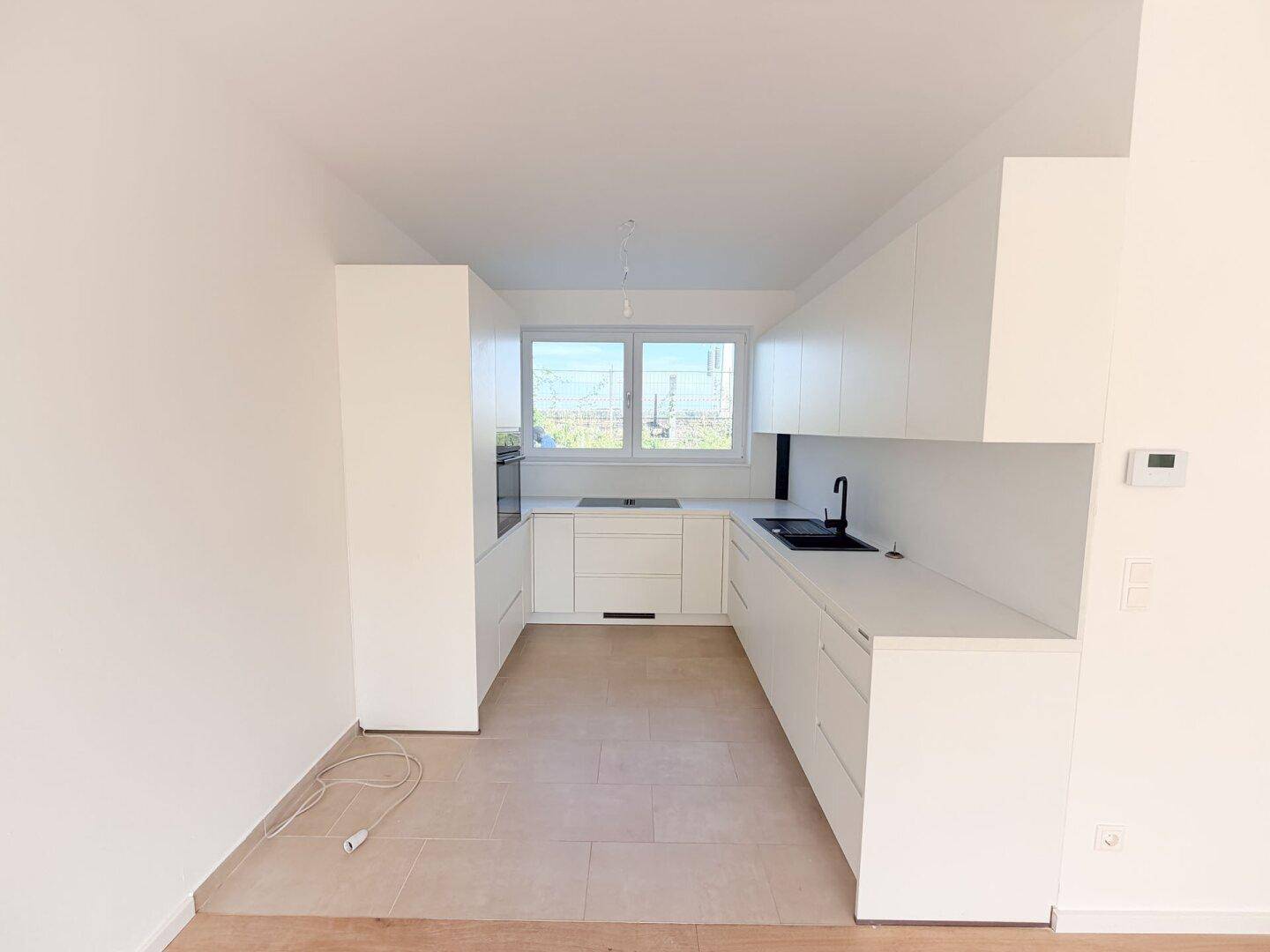 Funktionale Küche mit weißen Einbauschränken, integriertem Backofen und Fenster für Tageslicht.