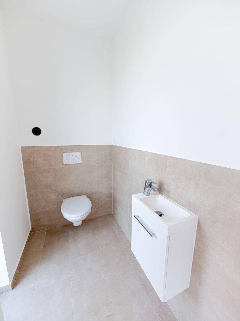 Modernes Gäste-WC mit wandhängender Toilette, kleinem Waschbecken und beigefarbenen Fliesen.