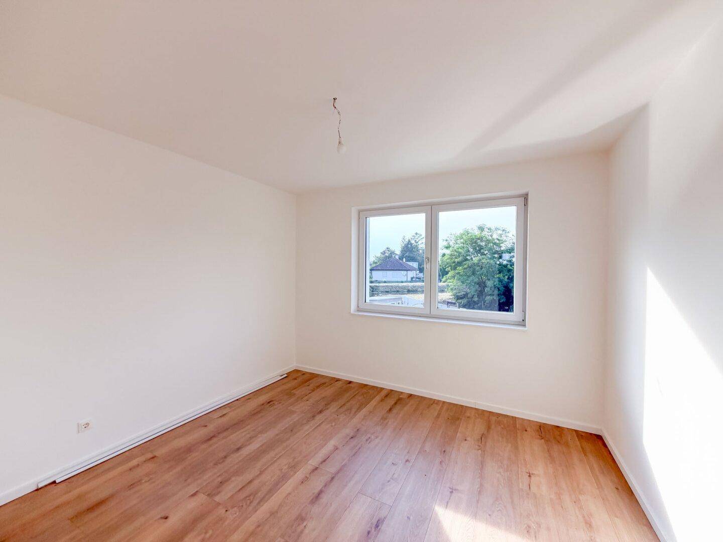 Helles Schlafzimmer mit Holzboden und Fenster mit Blick ins Grüne.