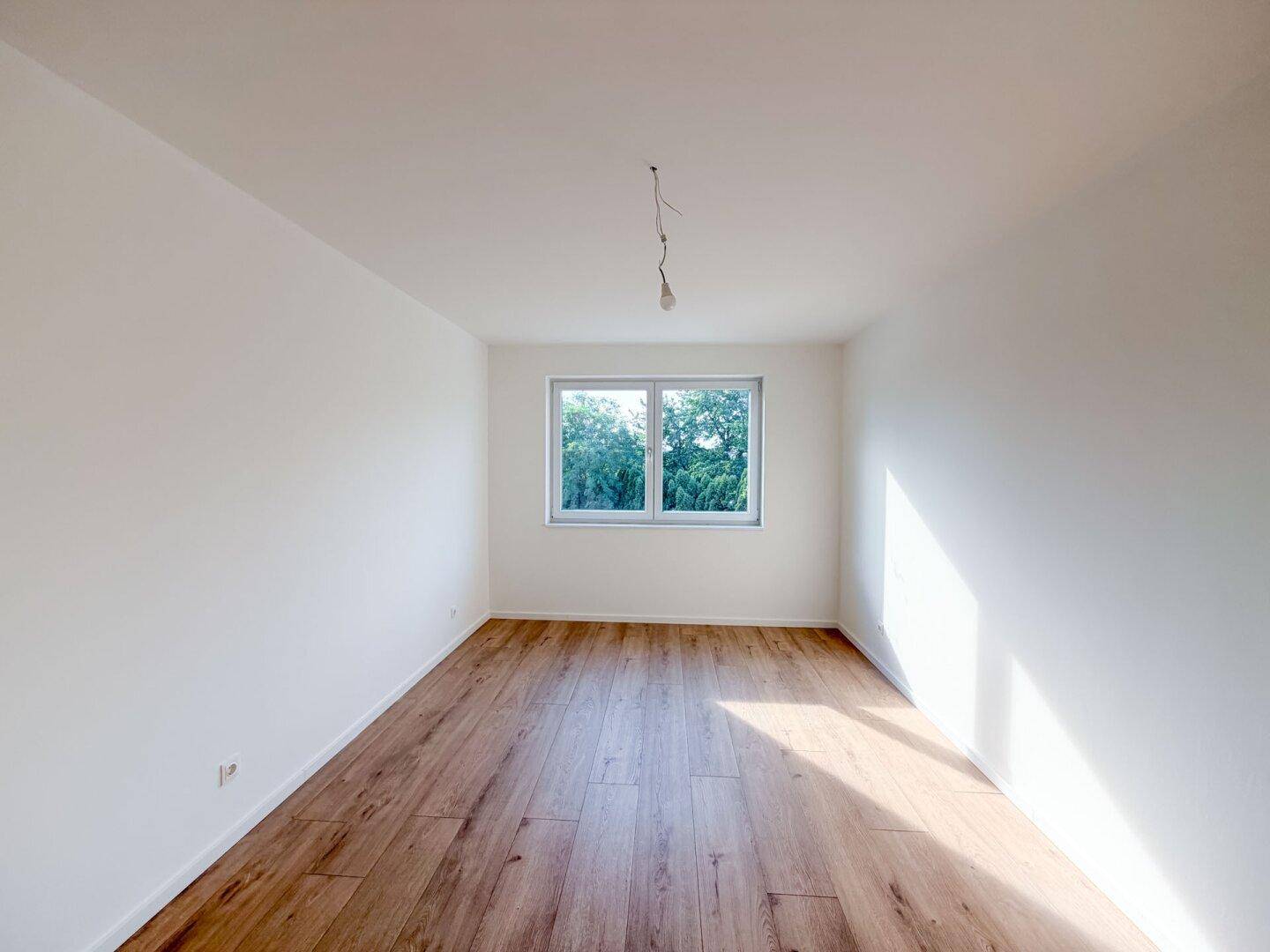 Geräumiges Schlafzimmer mit Holzboden und einem großen Fenster, das viel Sonnenlicht hereinlässt.