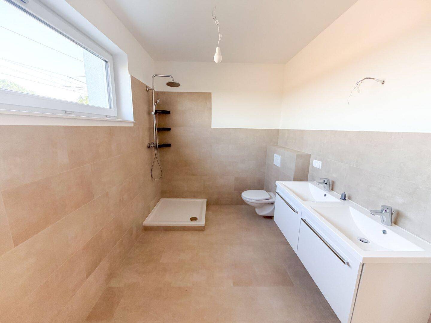 Modernes Badezimmer mit ebenerdiger Dusche, Doppelwaschbecken und Fenster für natürliche Belüftung.