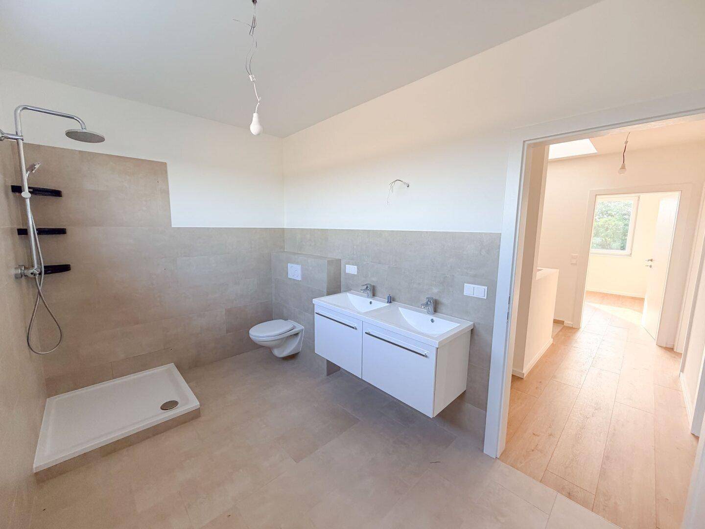 Geräumiges Badezimmer mit moderner Dusche, Doppelwaschbecken und hellen Fliesen.