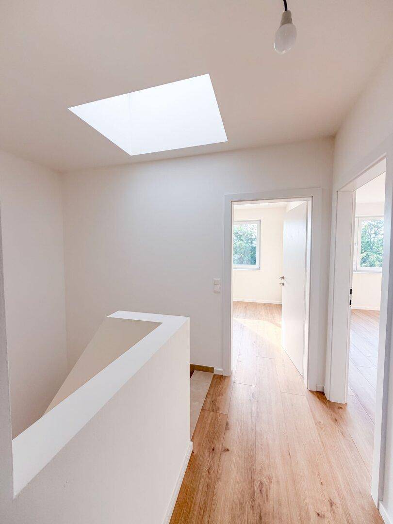Heller Flur im Obergeschoss mit Holzboden, Geländer und einem großen Oberlicht.