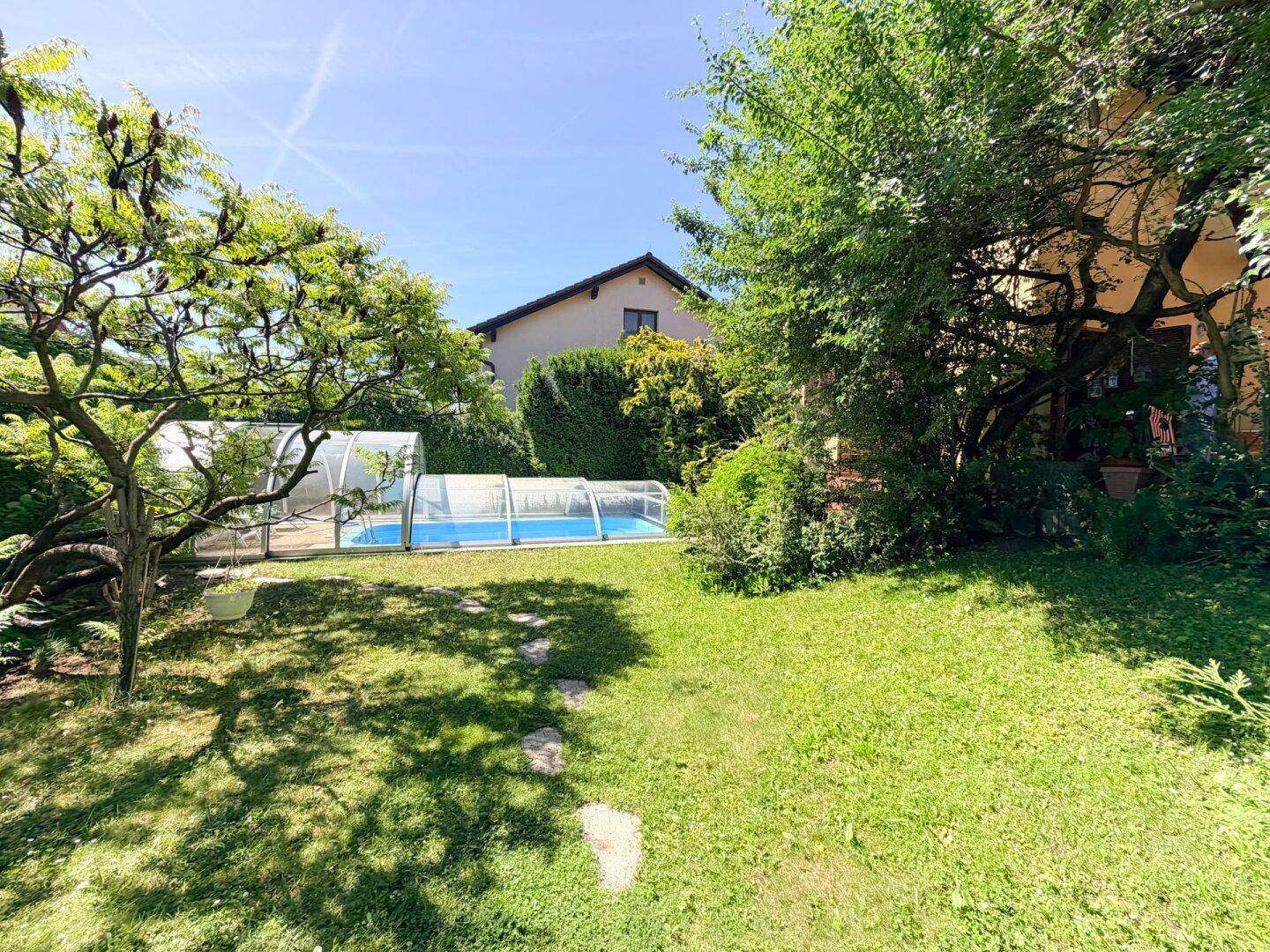 Weitläufiger Gartenbereich mit einem überdachten Pool und viel Grün, das Haus im Hintergrund.