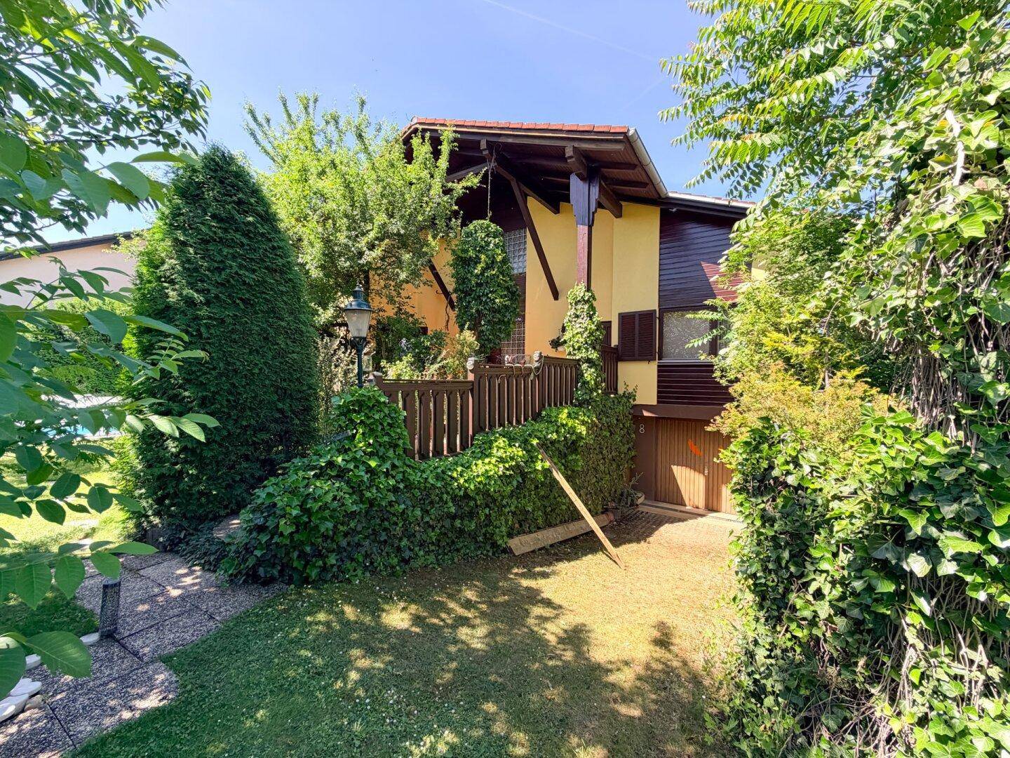 Seitlicher Eingangsbereich des Hauses mit Holzgeländer und üppigem Efeu, umgeben von viel Grün.