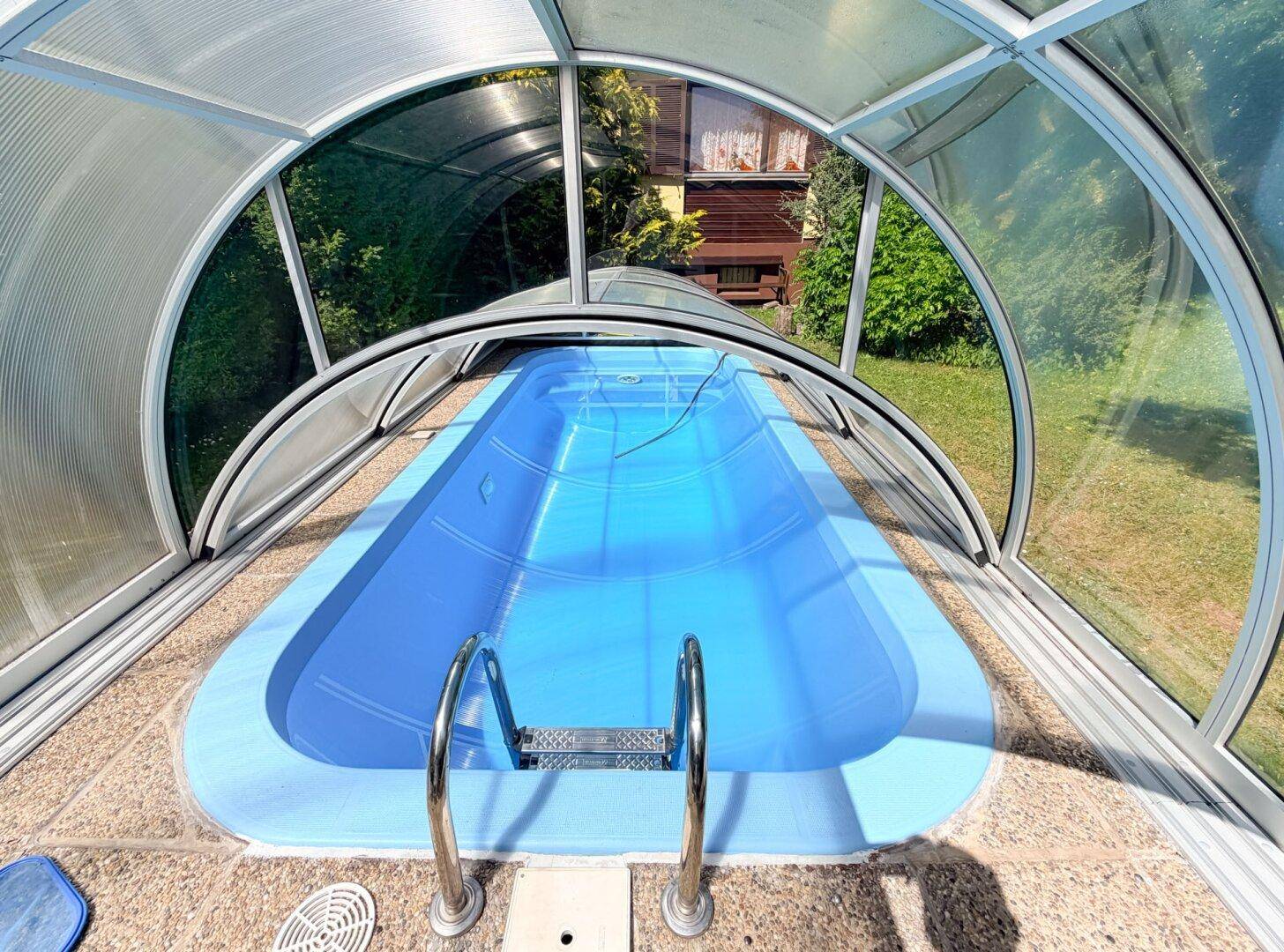 Nahaufnahme des überdachten Swimmingpools mit blauem Wasser und Einstiegsleiter an einem sonnigen Tag.