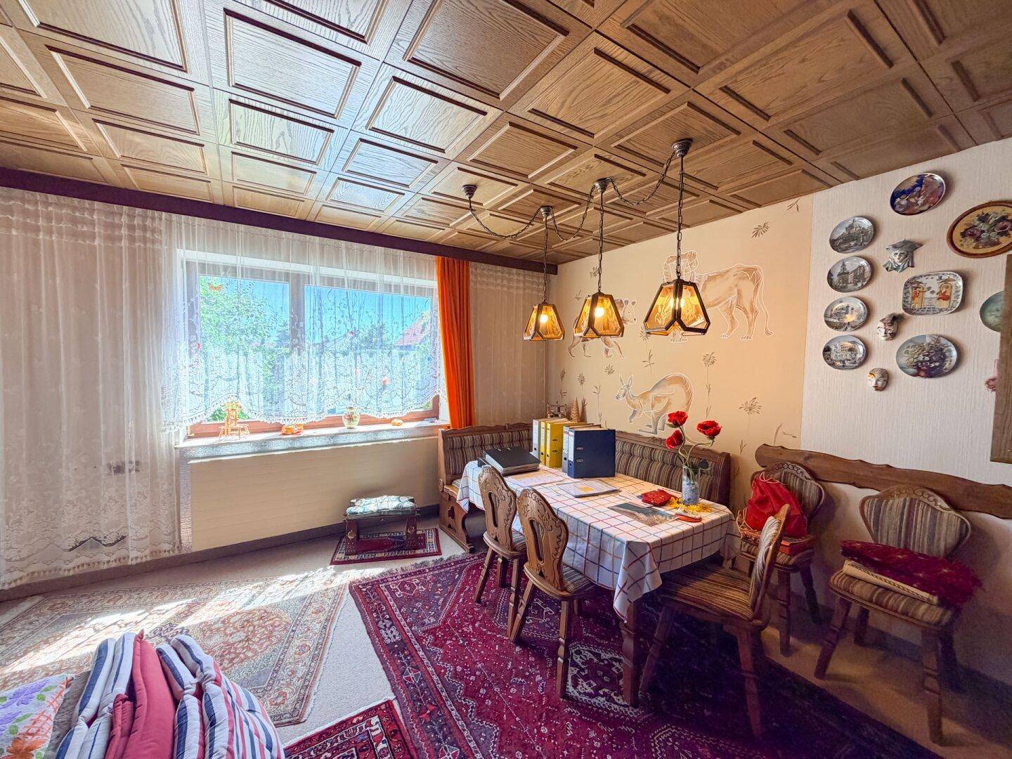 Gemütlicher Essbereich mit traditionellen Holzmöbeln, einer Kassettendecke und einem Fenster mit Vorhängen.