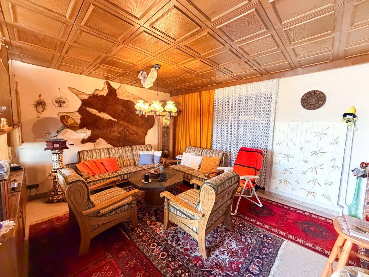 Traditionelles Wohnzimmer mit Holzmöbeln, einer Kassettendecke und einer auffälligen Tierfell-Wanddekoration.