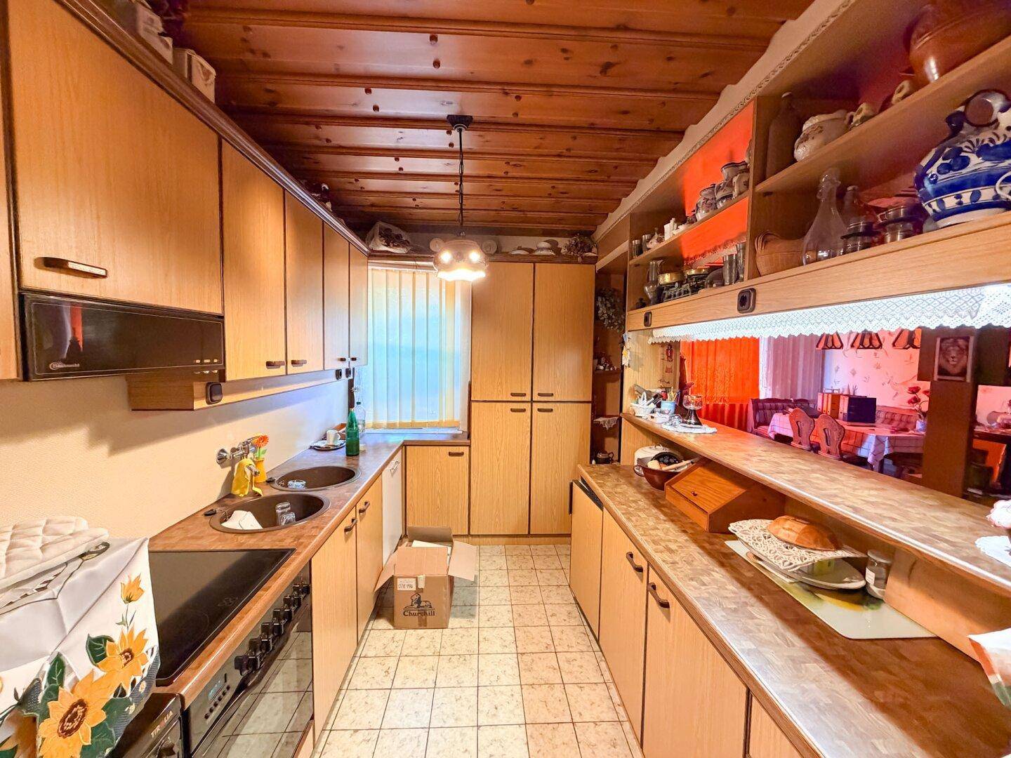 Funktionale Küche mit Holzschränken, Fliesenboden und einem Fenster, das Tageslicht hereinlässt.