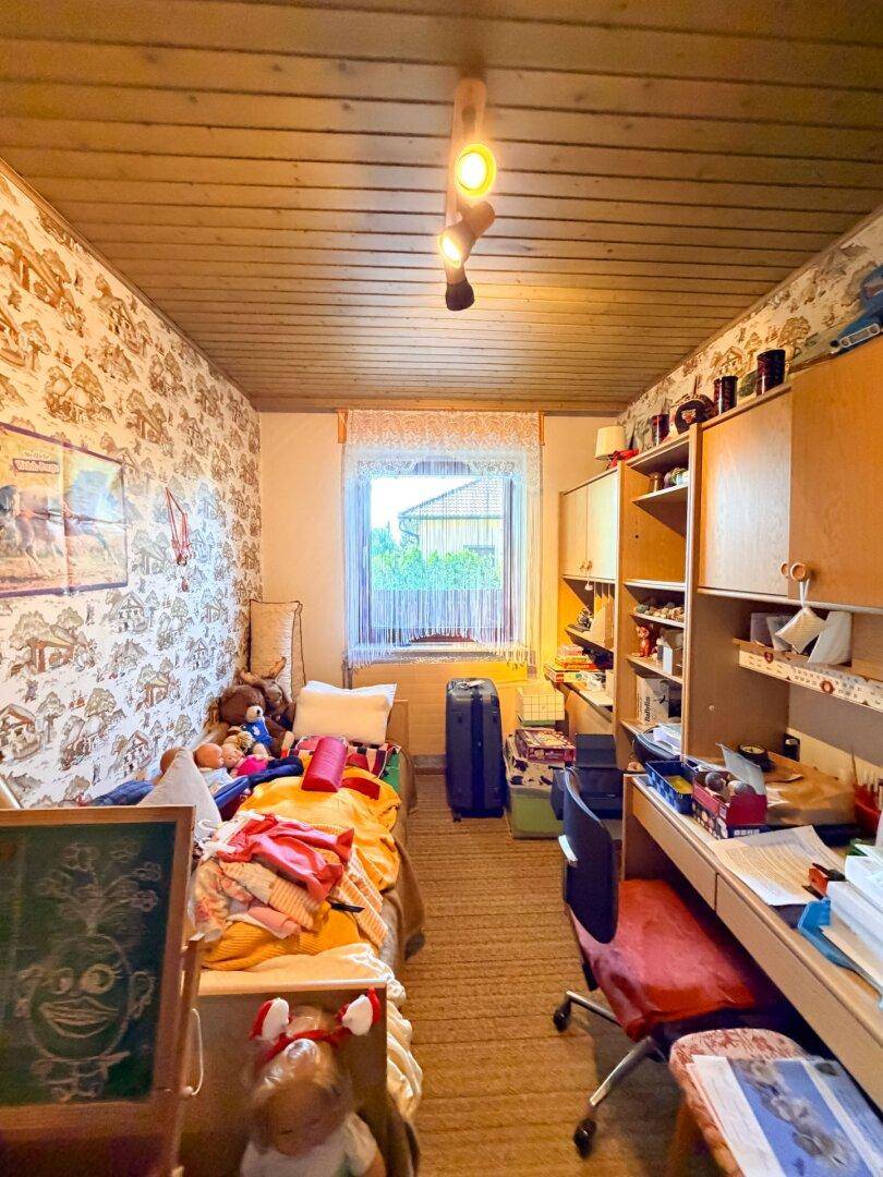 Kinder- oder Gästezimmer mit Einzelbett, Schreibtisch und Regalen, dekoriert mit Tapete.