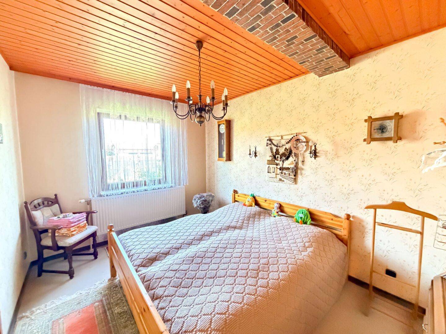 Schlafzimmer mit einem Holzbett, gemusterter Tapete und einer Holzdecke, die eine gemütliche Atmosphäre schafft.