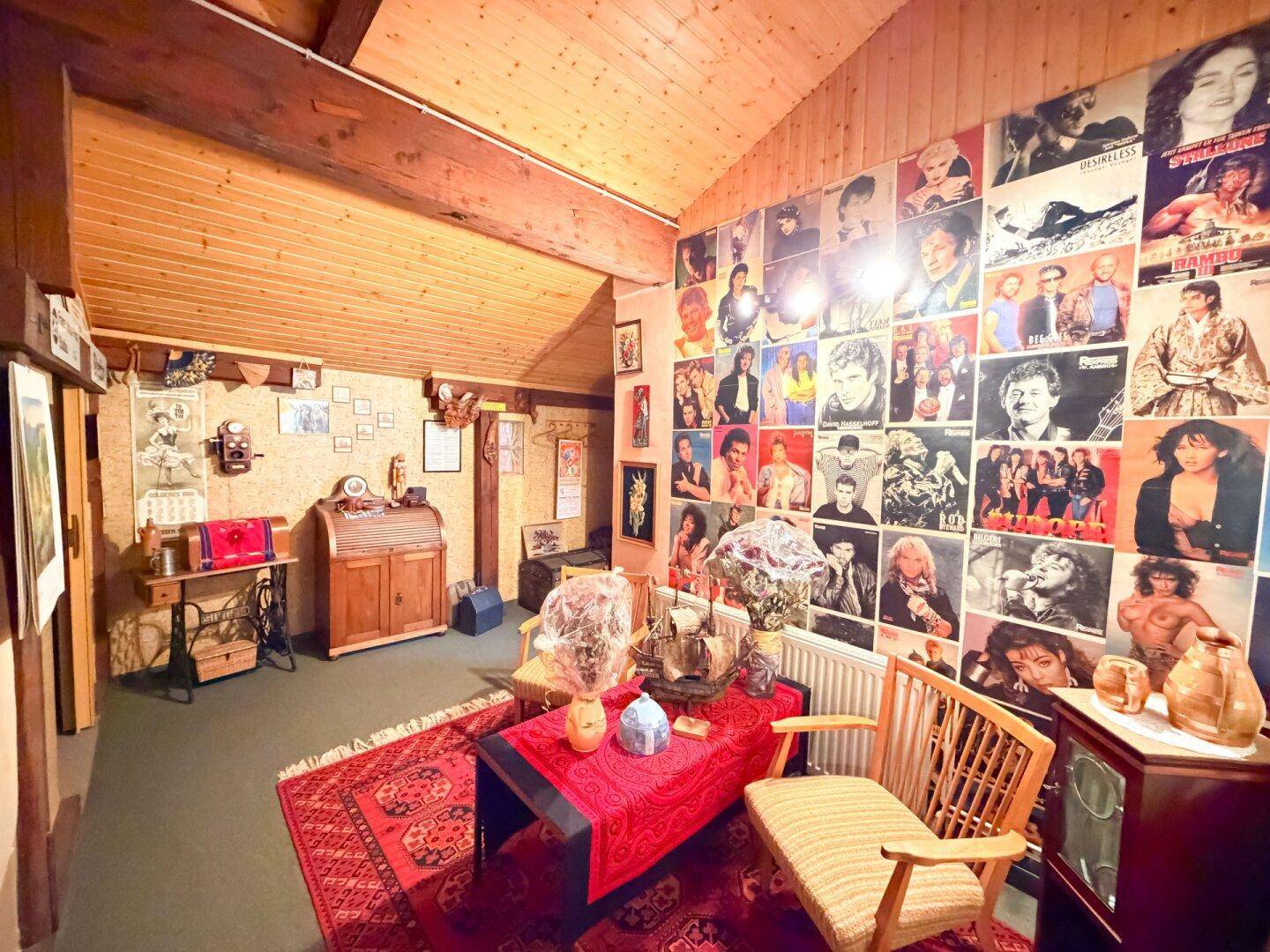 Dachzimmer mit schräger Holzdecke, dekoriert mit zahlreichen Postern und traditionellen Möbeln.