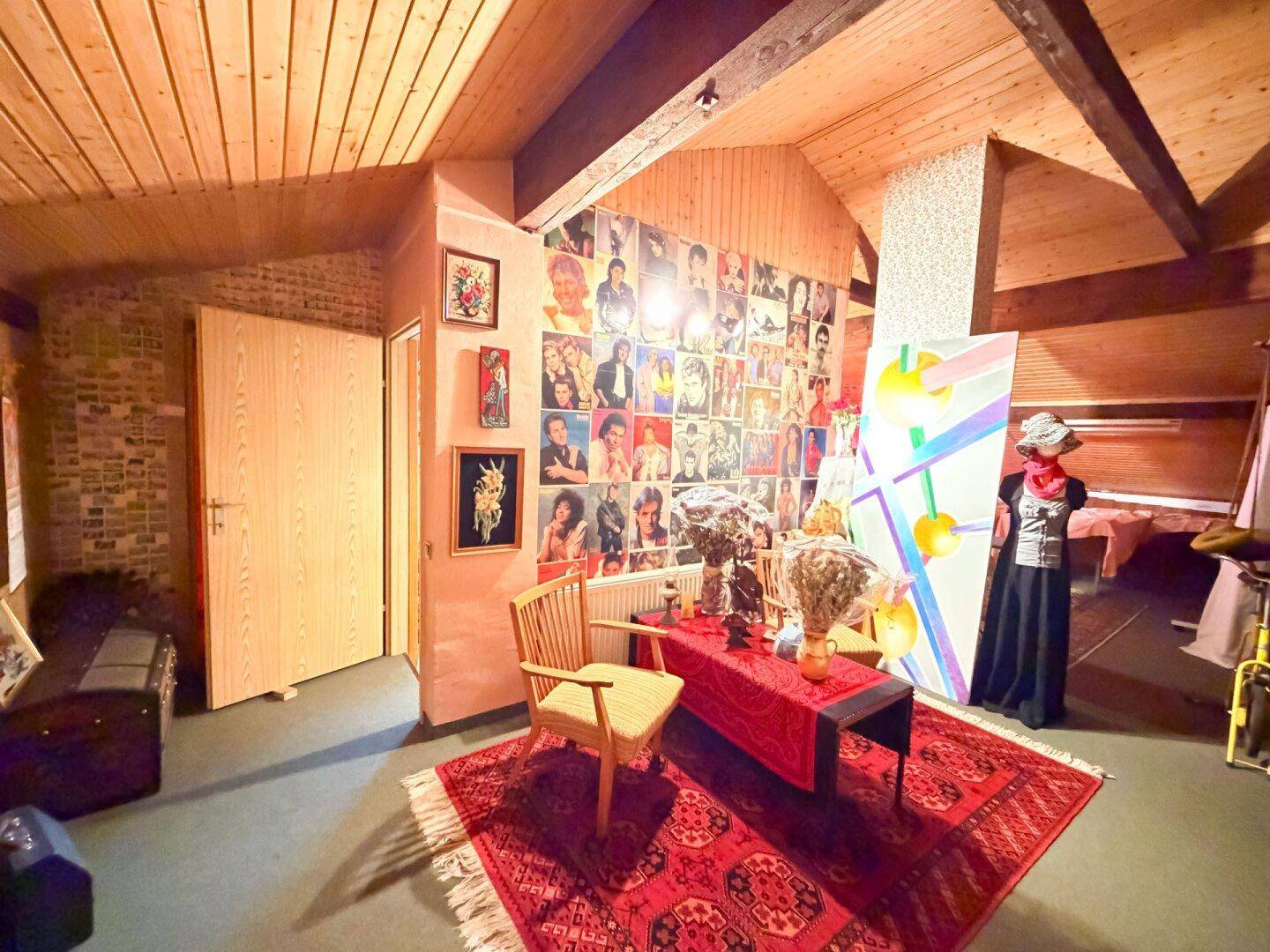 Weiterer Blick in das Dachzimmer mit schräger Holzdecke und einer Wand voller bunter Poster.