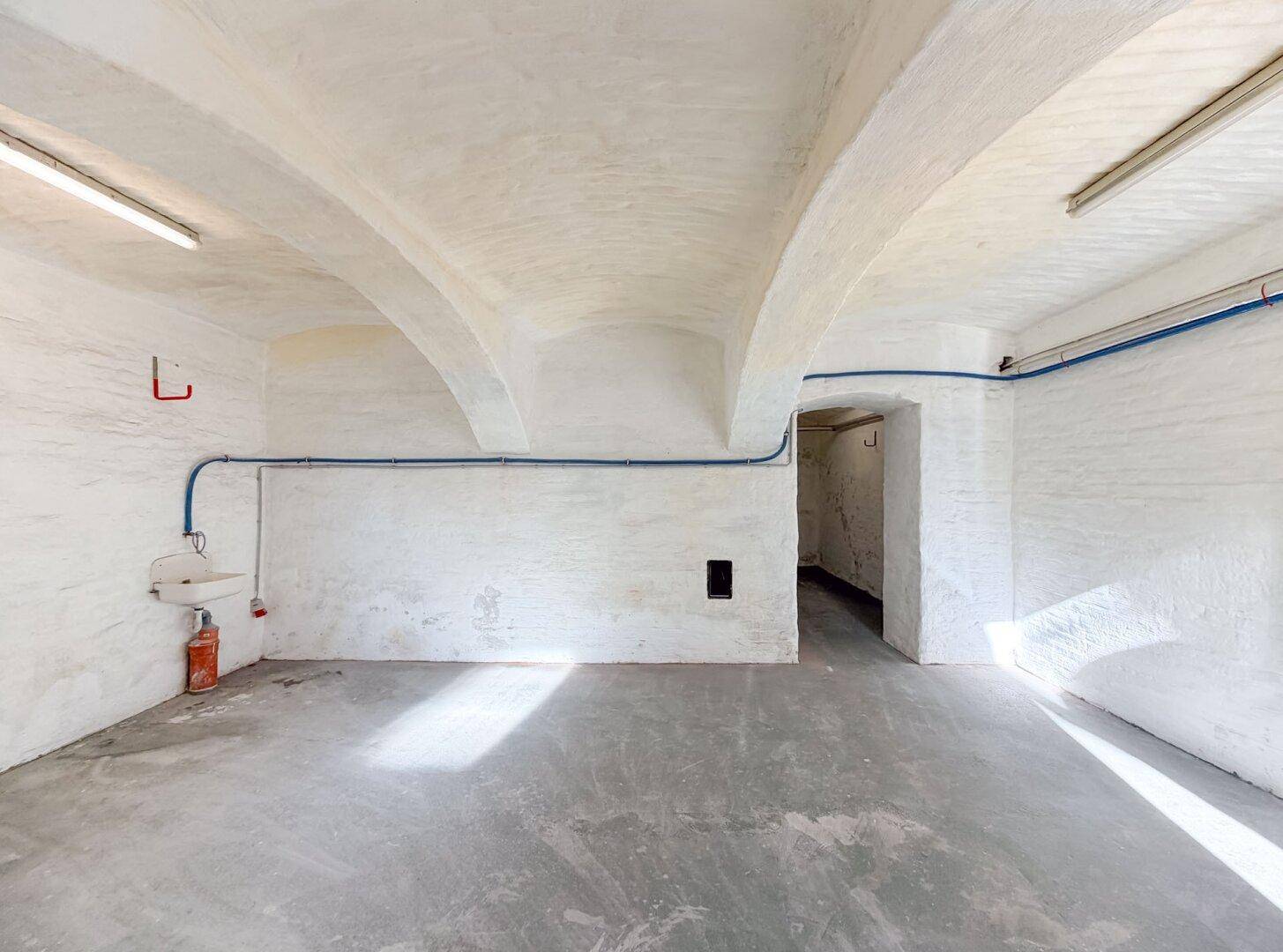 Geräumiger Kellerraum mit gewölbter Decke, weiß gestrichenen Wänden und einem kleinen Waschbecken.
