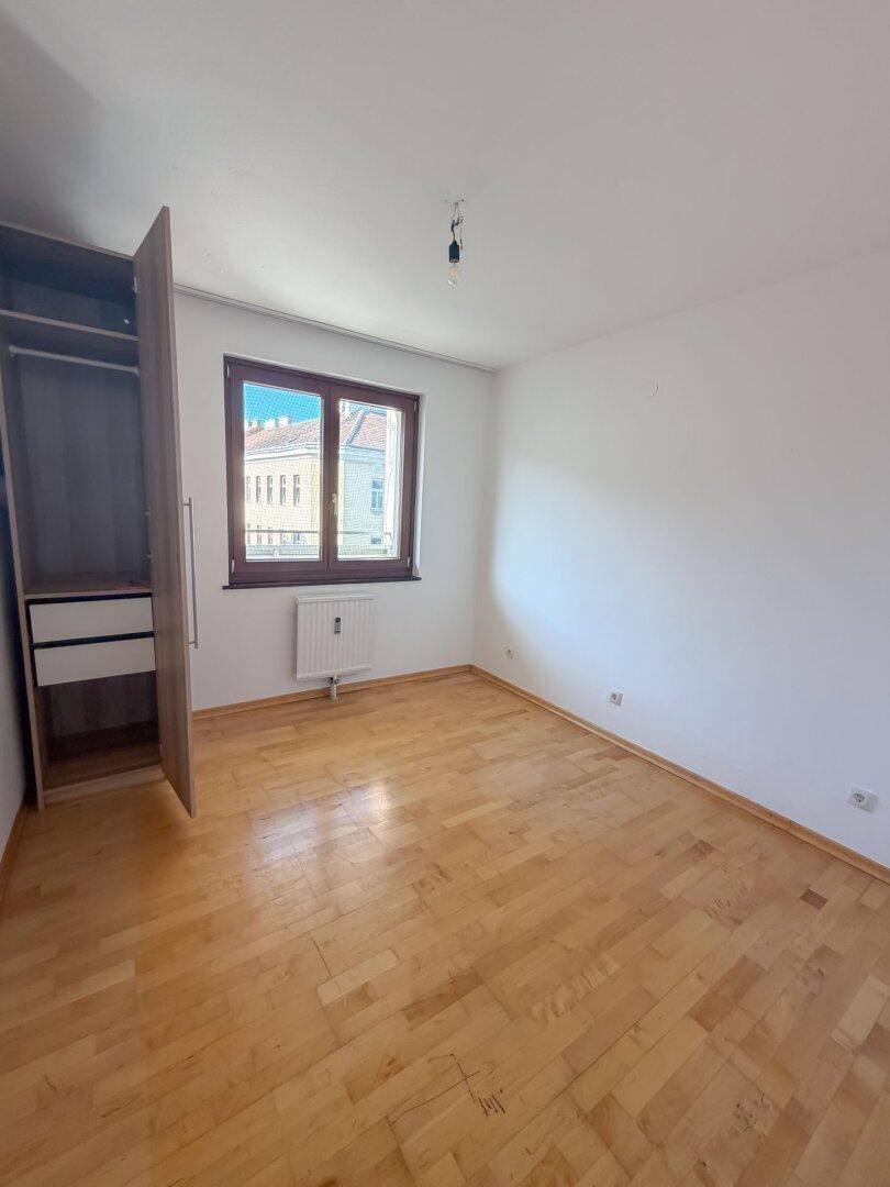 Schlafzimmer mit Parkettboden und einem Fenster, das Tageslicht hereinlässt.