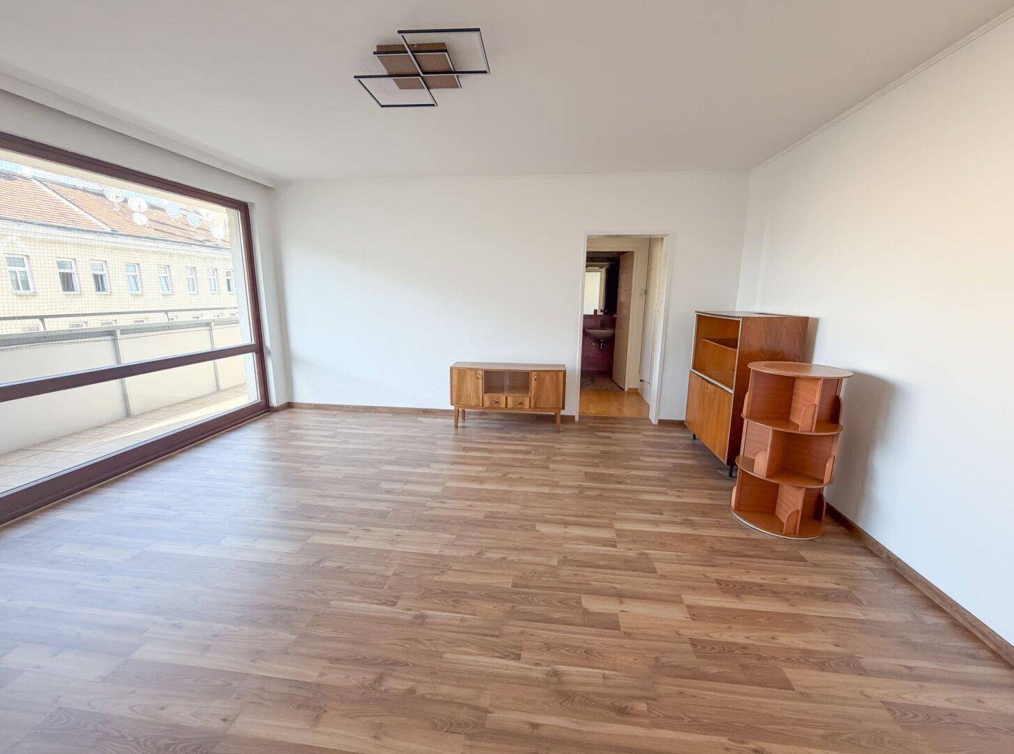 Geräumiges Wohnzimmer mit Laminatboden und Blick auf die umliegenden Gebäude.