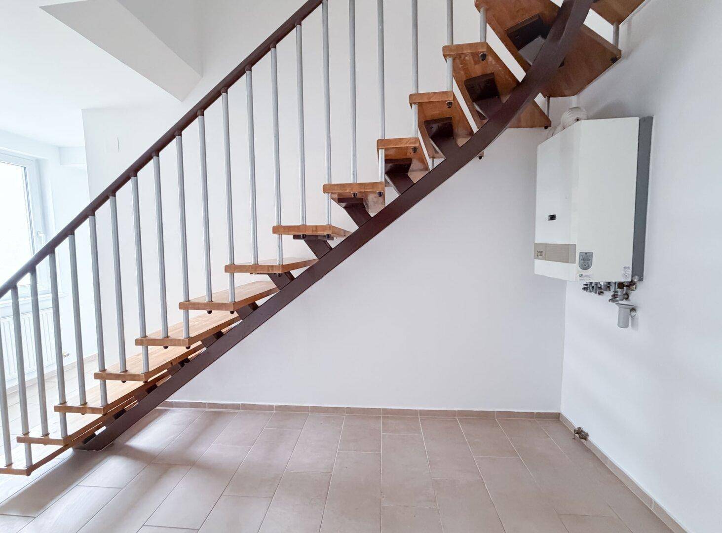 Detailansicht der Holztreppe mit Metallgeländer und einer Heizungsanlage an der Wand.