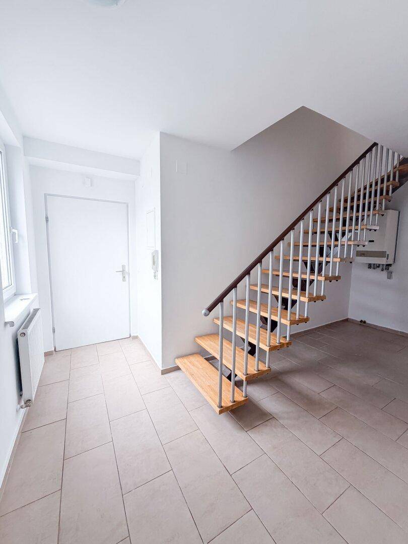 Heller Eingangsbereich mit Fliesenboden und einer modernen Holztreppe, die in die obere Etage führt.
