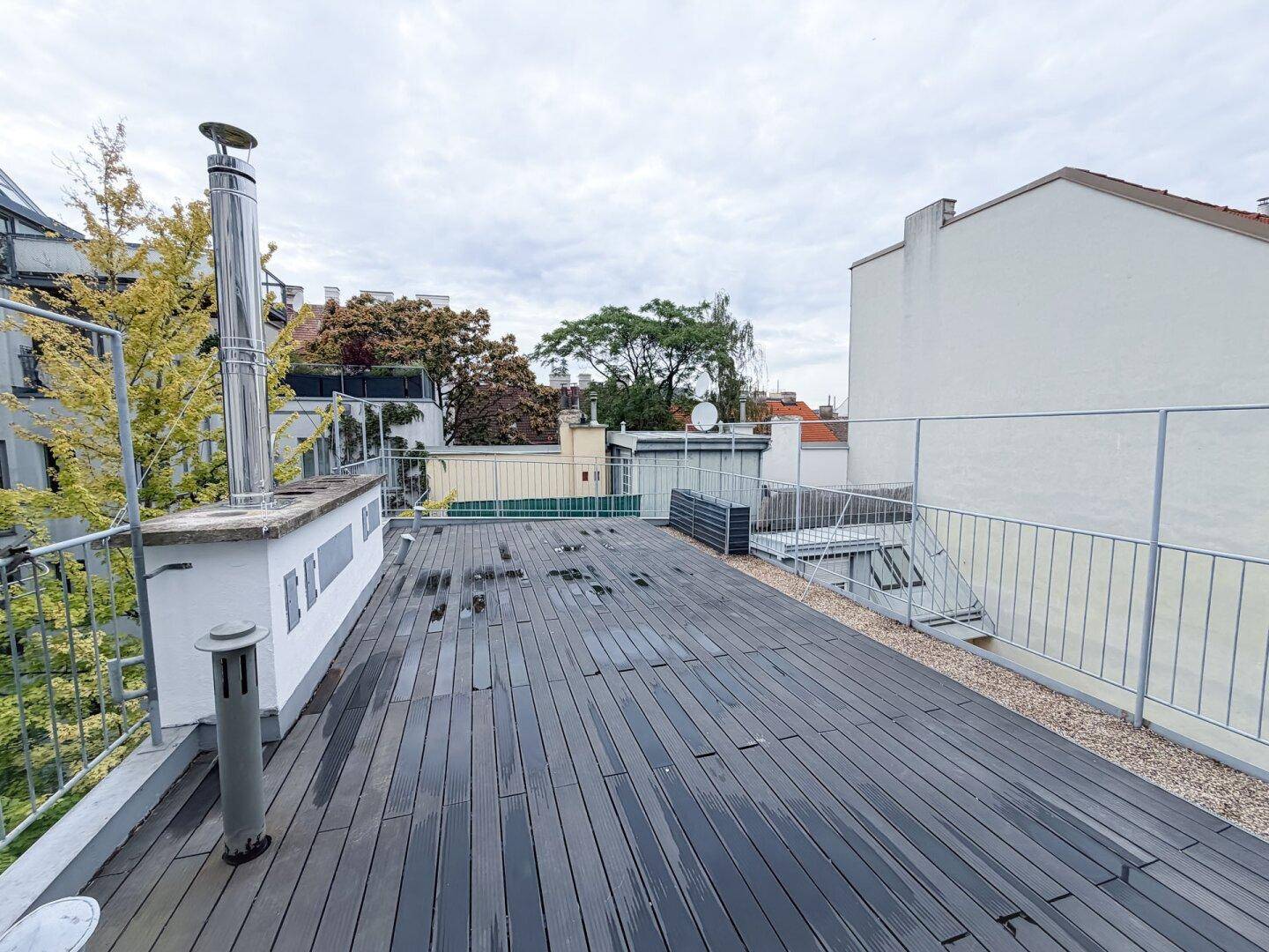 Geräumige Dachterrasse mit dunklem Holzbelag und Metallgeländer, umgeben von Stadtgebäuden.