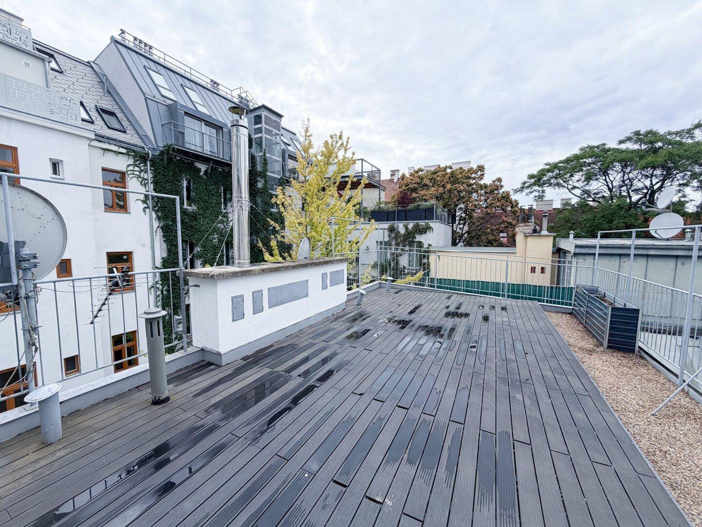 Große Dachterrasse mit dunklem Bodenbelag und Blick auf die benachbarten Gebäude und Bäume.