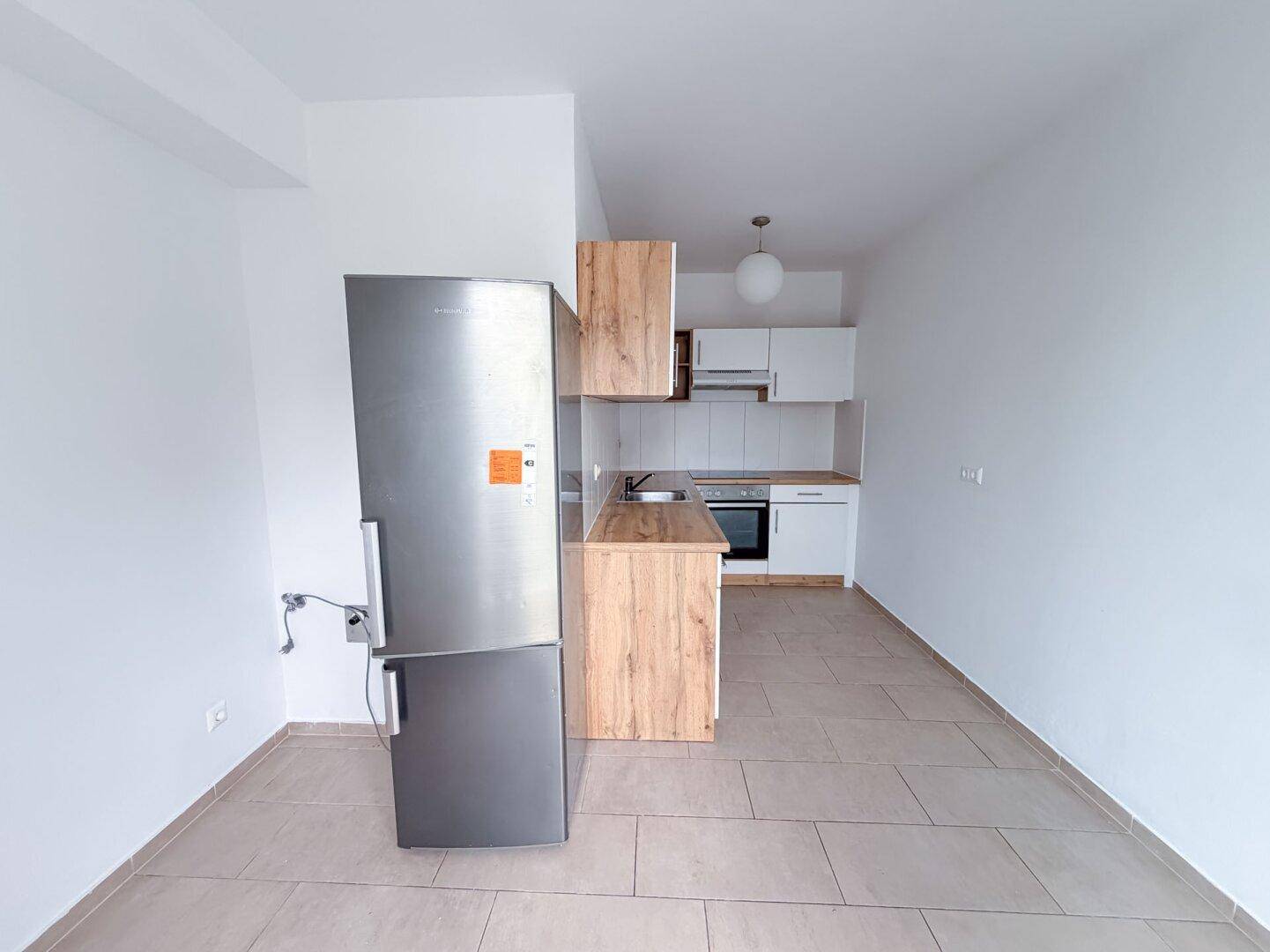 Offene Küche mit weißer Einrichtung, Holzdetails und einem freistehenden Kühlschrank.