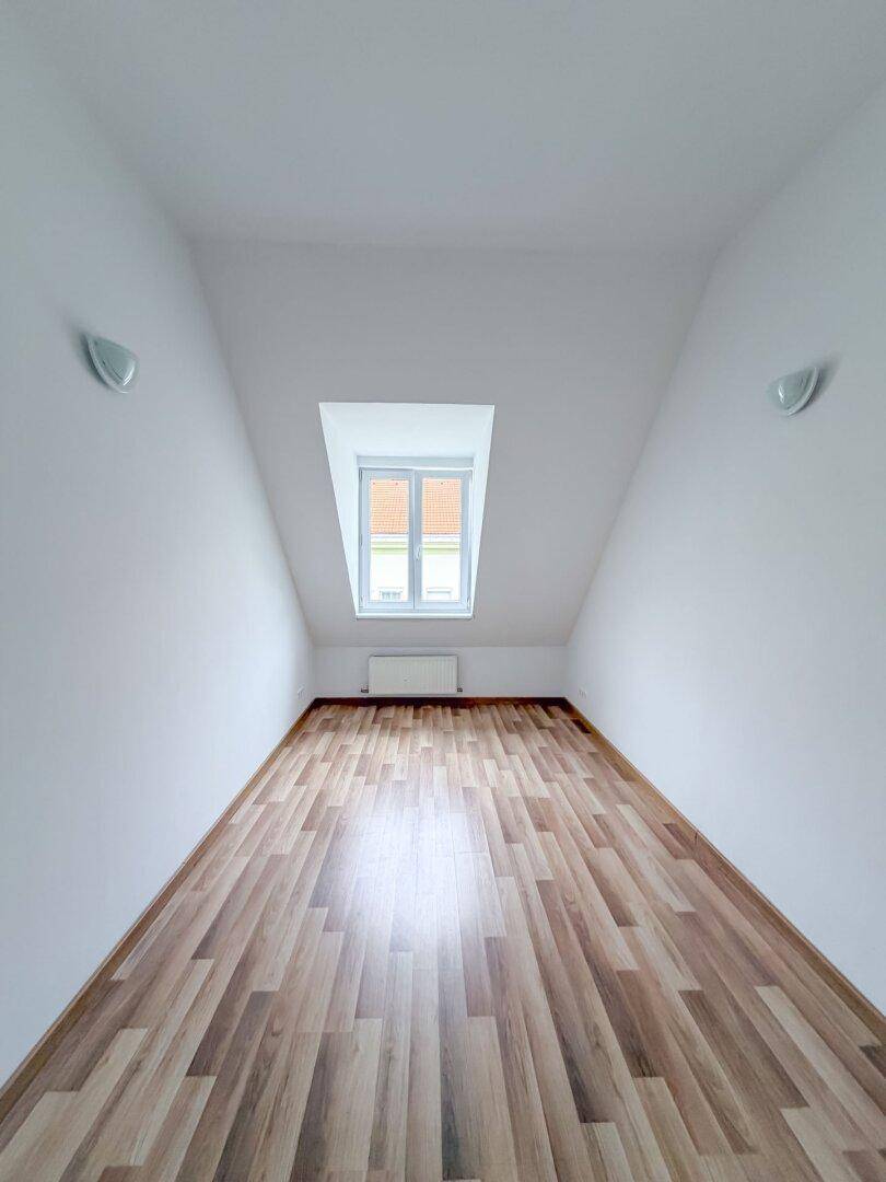 Dachgeschosszimmer mit Laminatboden, schrägen Wänden und einem Fenster, das viel Licht hereinlässt.