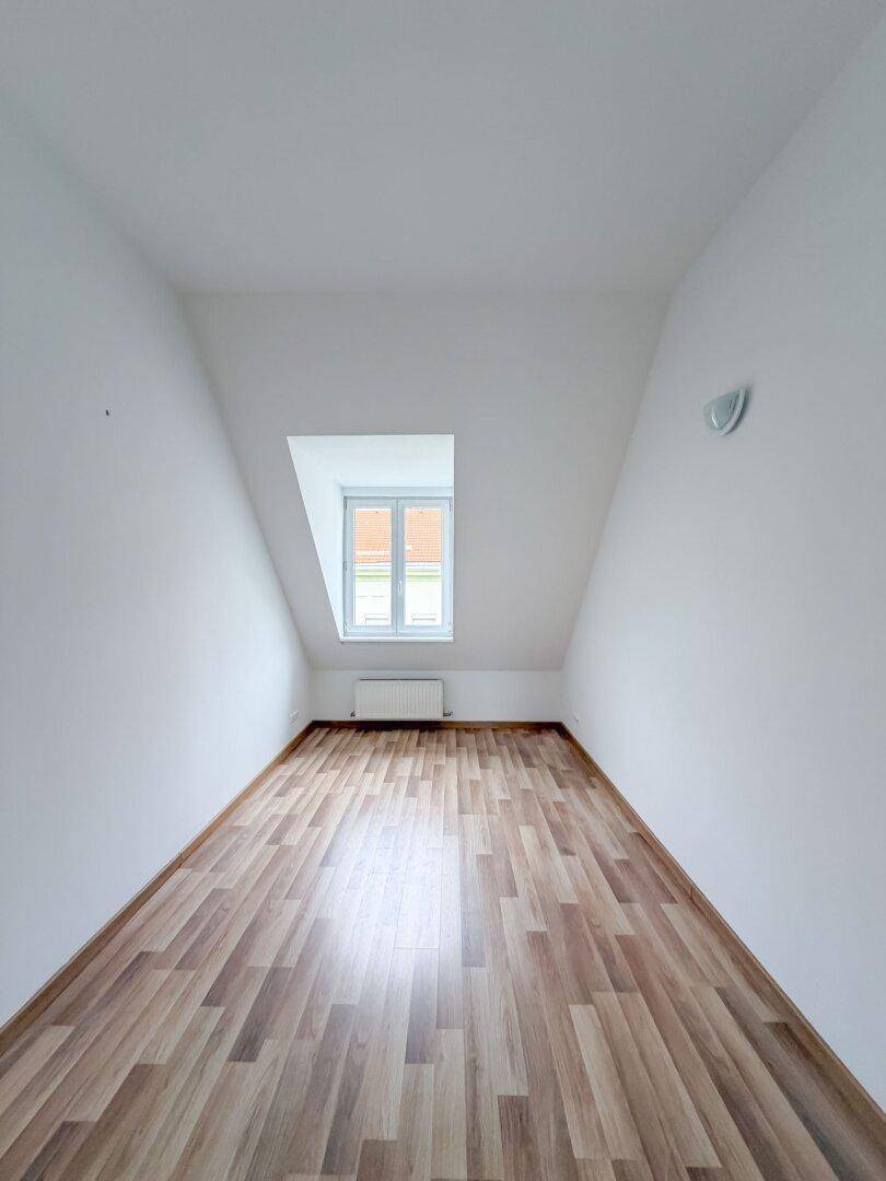 Helles Schlafzimmer im Dachgeschoss mit Laminatboden, Dachschräge und einem Gaubenfenster.