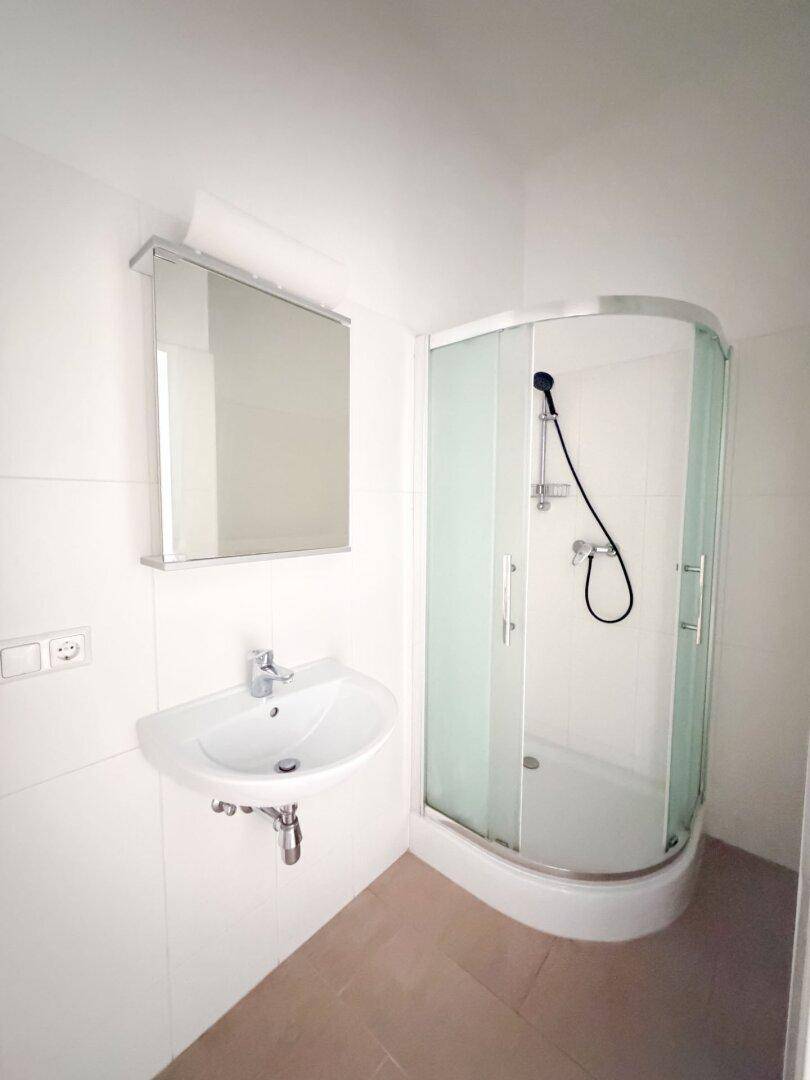 Kompaktes Badezimmer mit Eckduschkabine, Waschbecken und Spiegelschrank, hell gefliest.