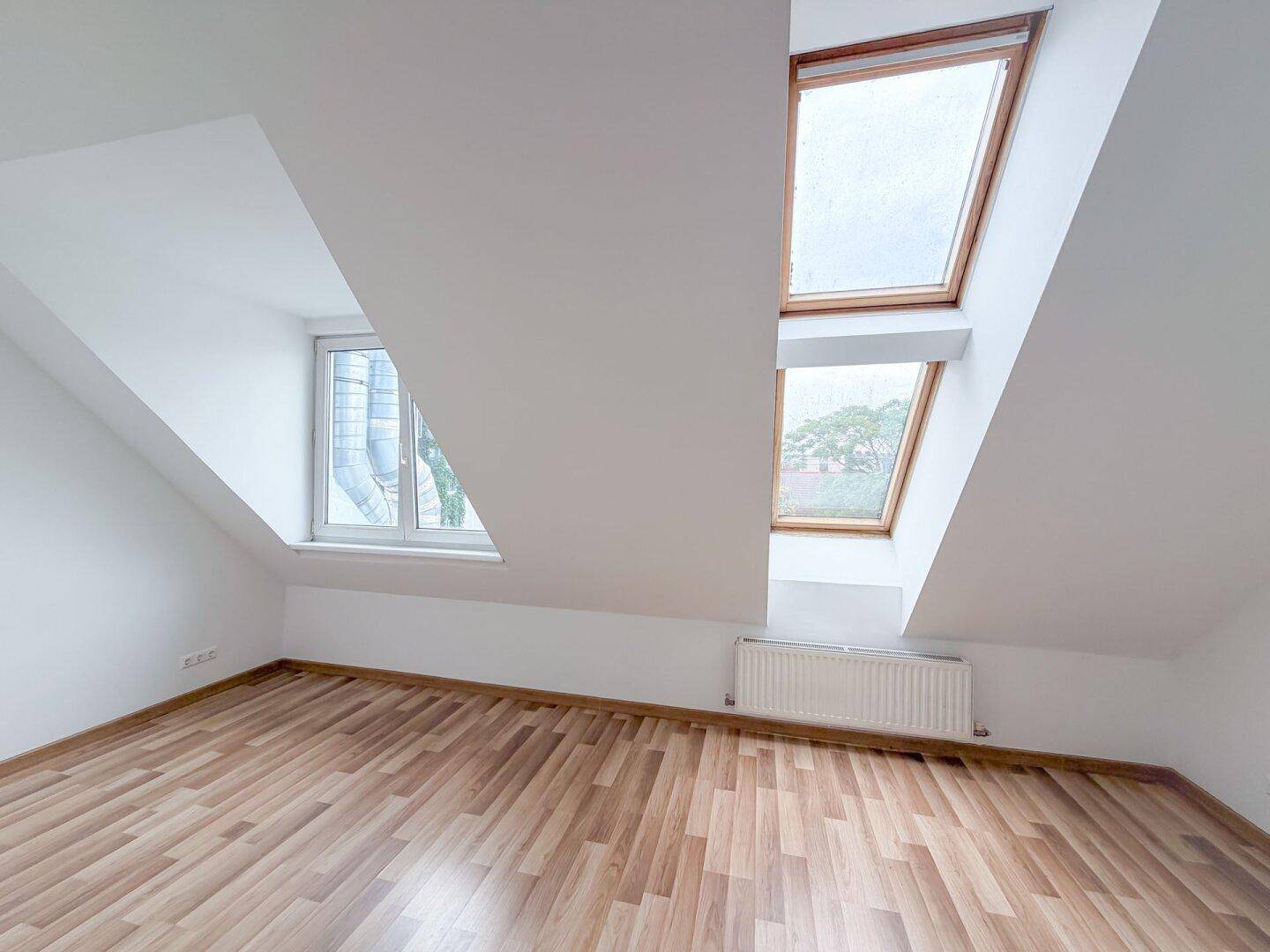 Helles Dachgeschosszimmer mit Laminatboden, Dachschrägen und mehreren Fenstern, inklusive Dachfenstern.