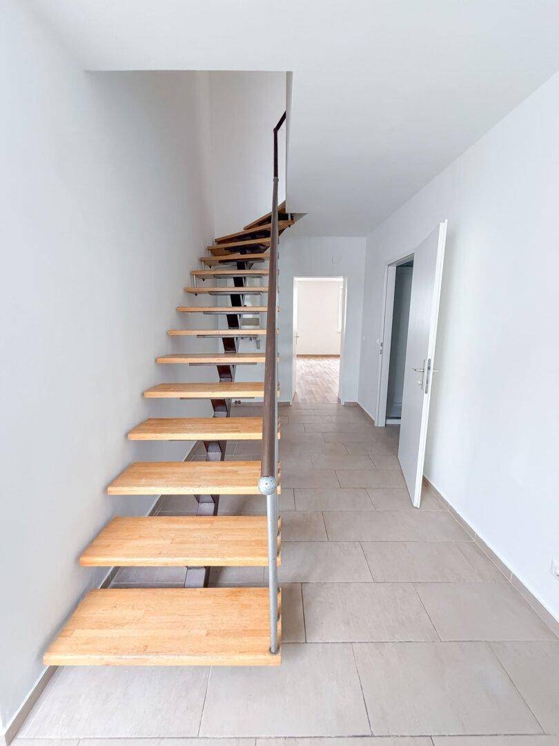 Heller Flur mit Fliesenboden und einer eleganten Holztreppe, die zu den oberen Etagen führt.